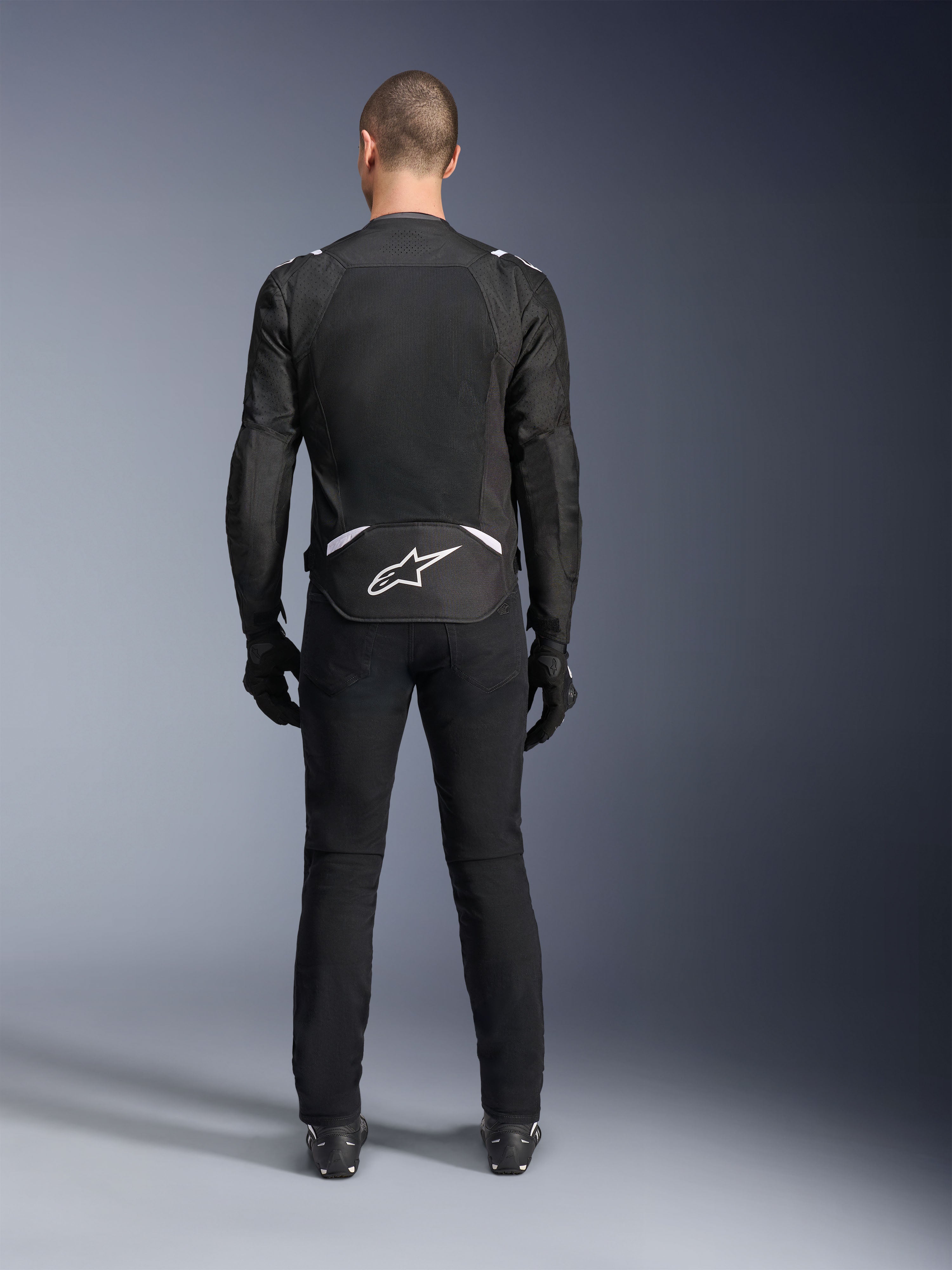 Alpinestars T-Sps Air V2 Jacket, Rear View, Black and White textile motorcycle jacket, featuring a large mesh back panel for maximum airflow and white Astars logo on the lower back, worn with black riding pants and gloves