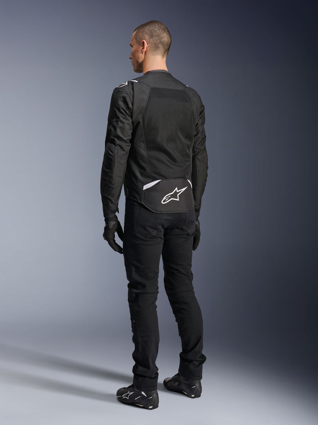 Alpinestars T-Sps Air V2 Jacket, Textile Motorcycle Jacket, Black, rear view showing large mesh ventilation panel and white Alpinestars logo on the lower back, paired with black riding pants and gloves for a sporty urban look.