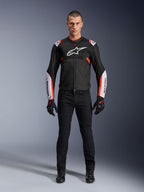 Modèle masculin portant la veste Alpinestars T-Sps Air V2 en Noir Blanc Rouge Fluo, dotée de larges panneaux en mesh technique et d'un logo blanc sur la poitrine et les manches, associée à un pantalon de moto technique et des gants noirs, équipement de moto sport urbain