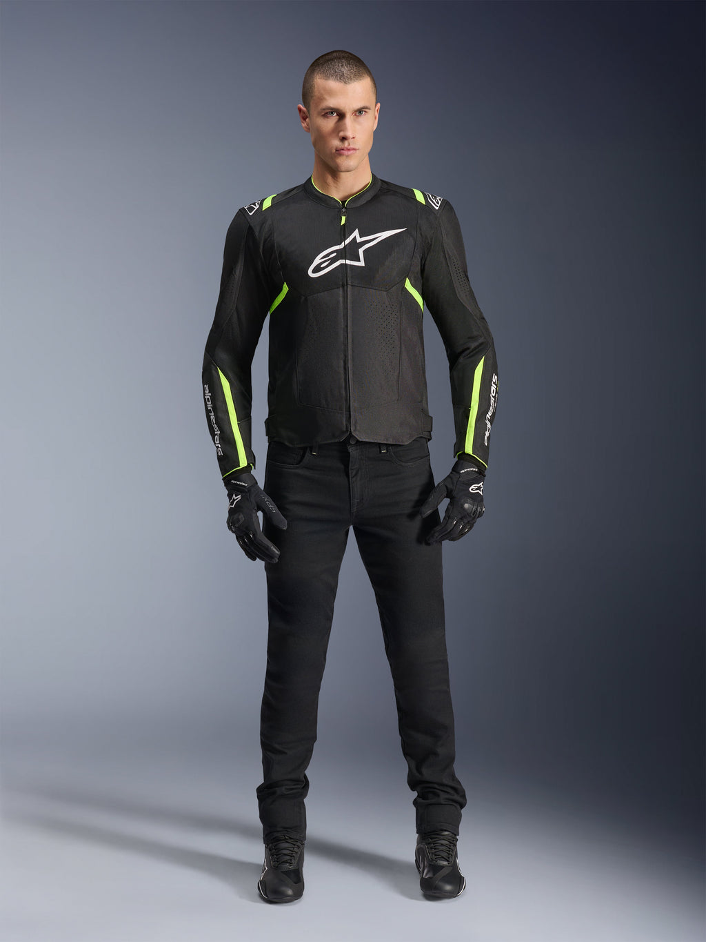 Veste Alpinestars T-Sps Air V2, noir et jaune fluo, veste de moto en textile avec panneaux en mesh, portée par un mannequin homme avec pantalon et gants noirs, arborant le logo Alpinestars blanc sur la poitrine, équipement de conduite sport urbain