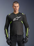 Veste Alpinestars T-Sps Air V2 en Noir Jaune Fluo, modèle masculin portant la veste textile ventilée avec panneaux en mesh et logo blanc sur la poitrine, associée à des gants de moto noirs, équipement de moto urbain
