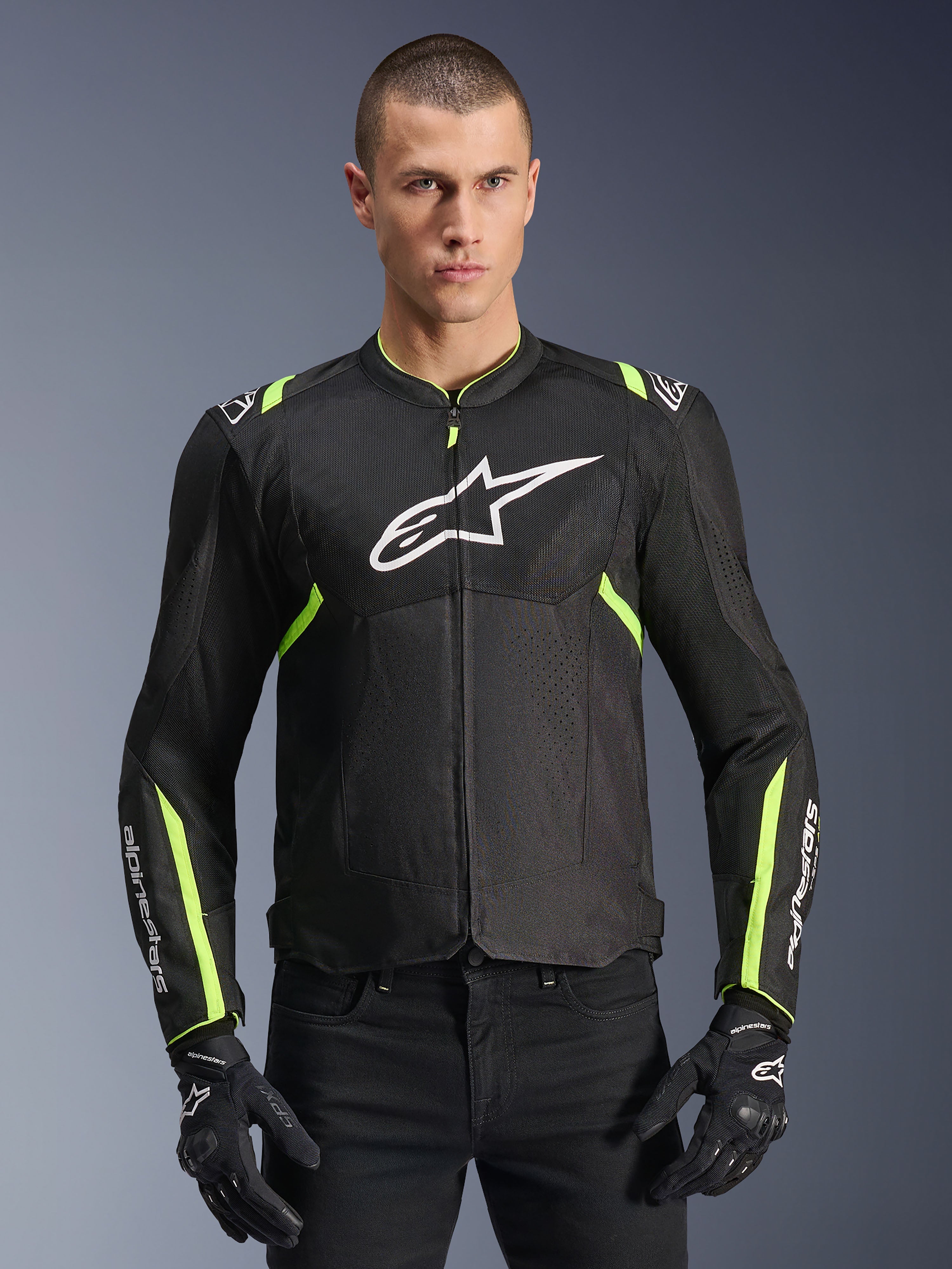 Veste Alpinestars T-Sps Air V2 en Noir Jaune Fluo, modèle masculin portant la veste textile ventilée avec panneaux en mesh et logo blanc sur la poitrine, associée à des gants de moto noirs, équipement de moto urbain