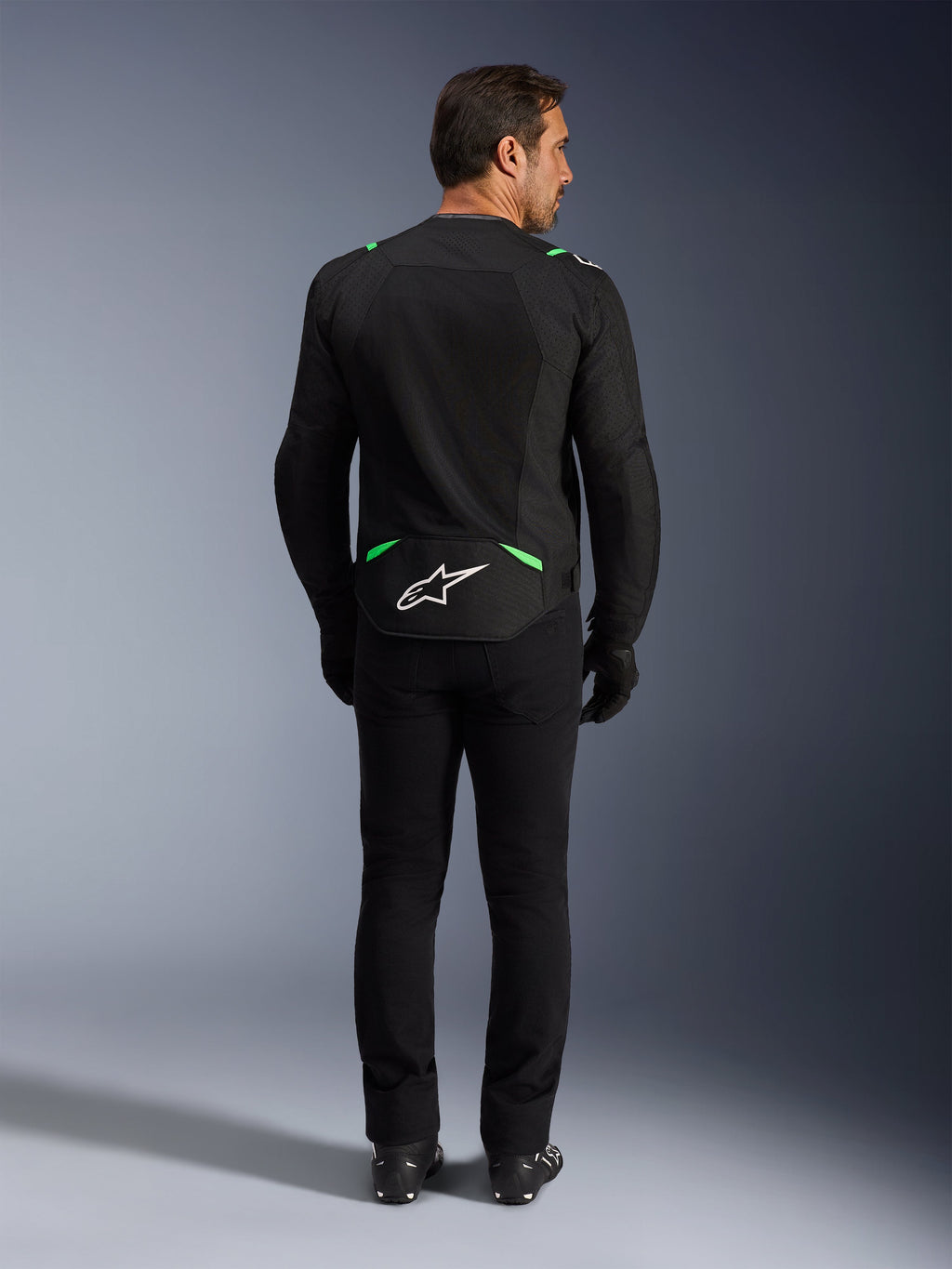 Veste Alpinestars T-SPS Air V2, veste de moto, noir et vert fluo, vue arrière avec logo blanc sur le bas du dos, portée avec un pantalon et des bottes noirs assortis, conception en maille ventilée pour la conduite sportive