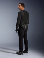 Un homme portant la veste Alpinestars T-SPS Air V2 en Noir Vert Fluo, présenté de dos et de profil, avec un pantalon de moto noir et des chaussures de moto. La veste présente des panneaux en maille technique ventilée, des accents vert vif sur les épaules et le bas du dos, ainsi qu'un logo étoile blanc à l'arrière.