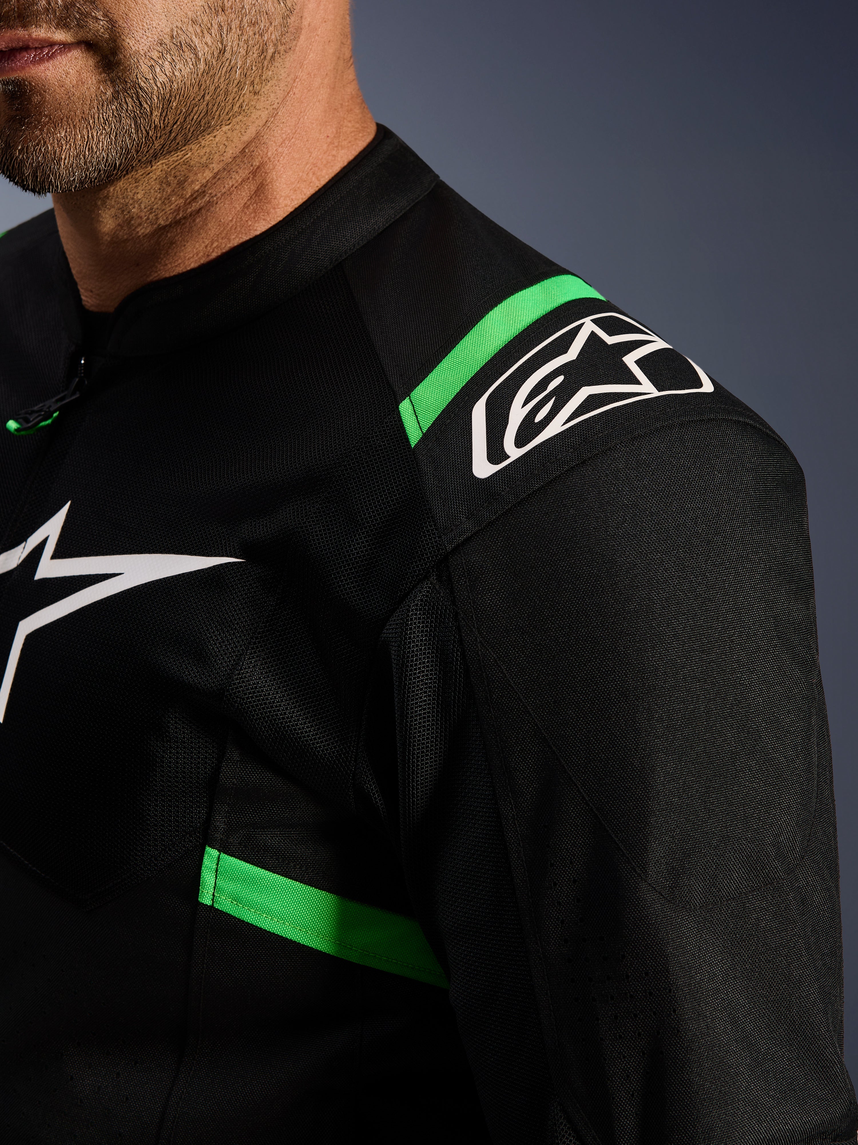 Veste Alpinestars T-SPS Air V2, noir et vert fluo, gros plan sur l'épaule et le torse, logo étoile Alpinestars blanc, maille technique pour la circulation de l'air, veste de moto sportive
