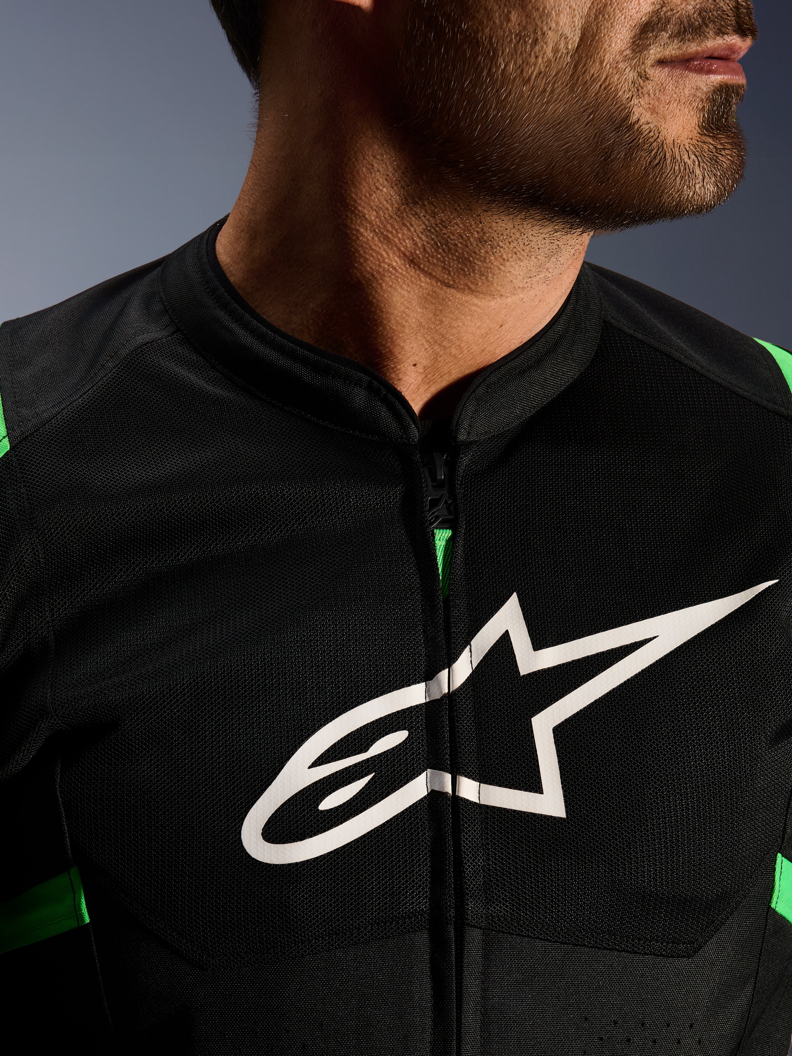 Gros plan de la veste Alpinestars T-SPS Air V2, noir et vert fluo, avec panneaux en maille technique respirante, fermeture éclair centrale et logo étoile Alpinestars blanc sur la poitrine, équipement moto haute performance