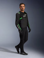 Modèle masculin portant une veste Alpinestars T-SPS Air V2 en noir et vert fluo, associée à un pantalon de moto et des gants noirs, veste textile coupe sport avec panneaux en maille et accents néon, tenue de moto urbaine complète