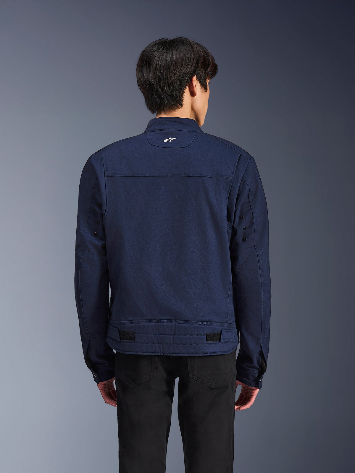 Veste Alpinestars Bruiser, veste de moto en textile bleu foncé, vue de dos sur mannequin, design d'inspiration workwear avec un petit logo Astars blanc sur la nuque, pattes de réglage à la taille, vêtement de moto urbain contemporain.