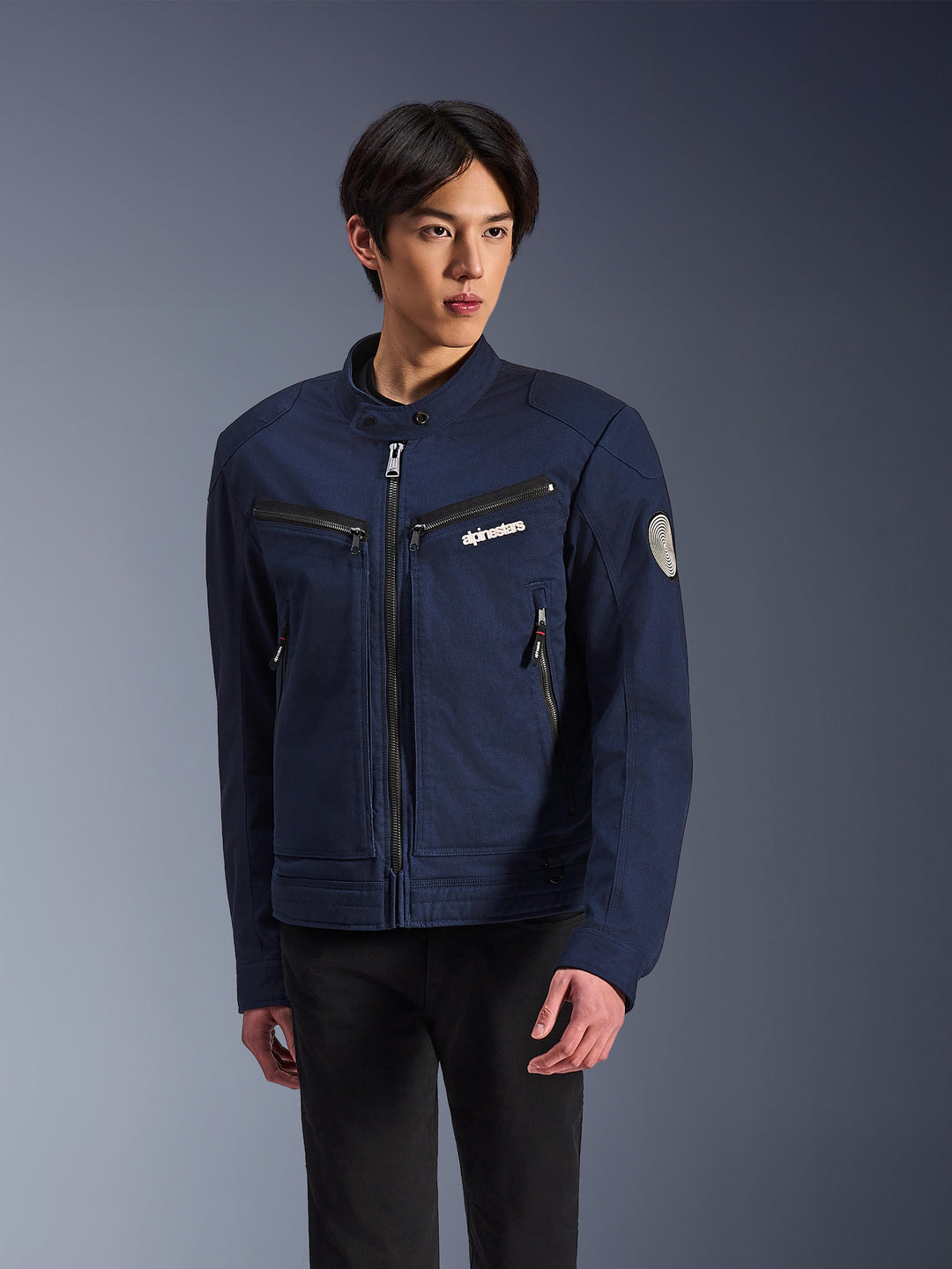 Alpinestars Bruiser Jacket, veste de moto urbaine pour homme, bleu marine avec fermetures éclair noires, logo sur la poitrine, patch circulaire sur la manche, poches zippées