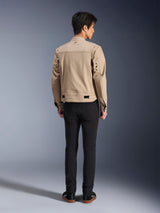 Vue arrière d'un mannequin portant la veste Alpinestars Bruiser marron, veste de moto urbaine au design inspiré du vêtement de travail, avec des œillets métalliques au dos et des ajusteurs à la taille, associée à un pantalon noir et des baskets, style urbain contemporain.
