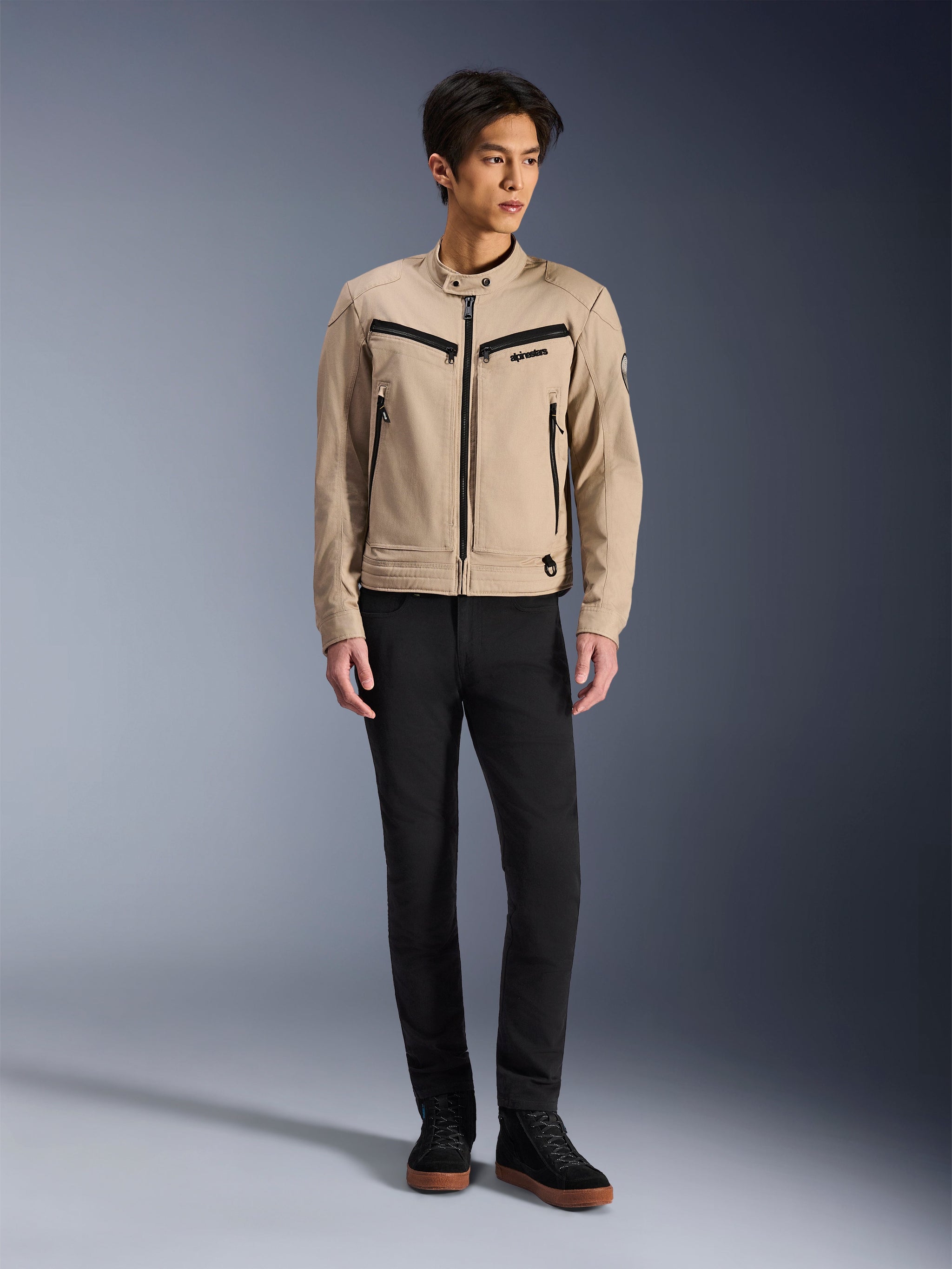 Veste Alpinestars Bruiser, veste de moto urbaine en Aluminum, portée avec un pantalon noir et des baskets noires, dotée de poches zippées noires et d'un col à bouton-pression, design contemporain inspiré du vêtement de travail pour la conduite urbaine