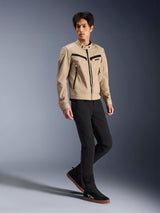 Veste Alpinestars Bruiser, veste de moto urbaine, beige, portée par un mannequin homme avec un pantalon slim noir et des baskets noires, construction textile inspirée du vêtement de travail avec des zips noirs contrastés, style urbain contemporain.
