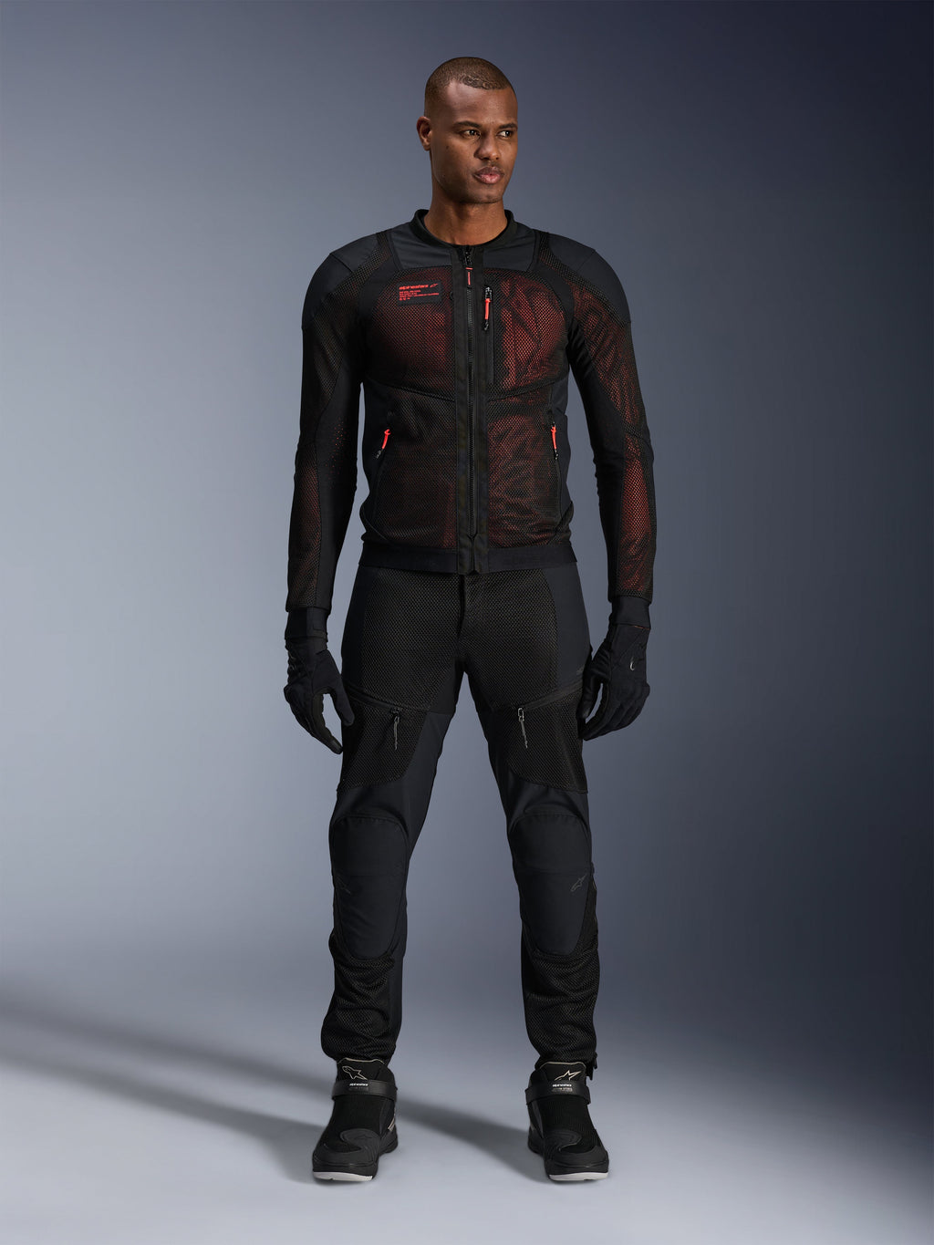 Veste Alpinestars Troop-Air Pro, veste technique aérée avec protections, Noir et Rouge Fluo, portée par un mannequin homme avec pantalon et gants de moto assortis, dotée de panneaux en mesh haute ventilation et d'accents rouges, équipement de moto urbain