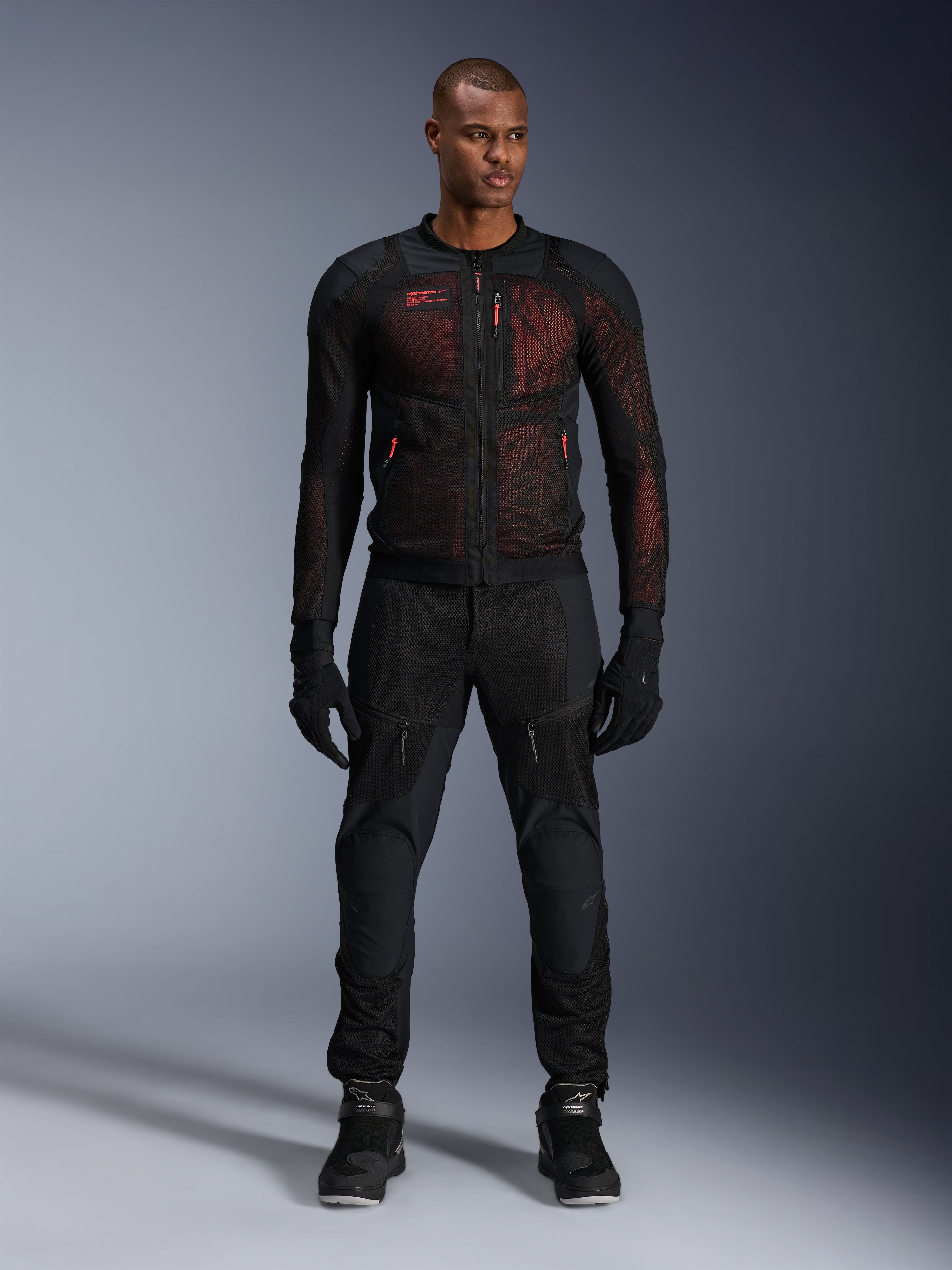 Veste Alpinestars Troop-Air Pro, veste technique aérée avec protections, Noir et Rouge Fluo, portée par un mannequin homme avec pantalon et gants de moto assortis, dotée de panneaux en mesh haute ventilation et d'accents rouges, équipement de moto urbain