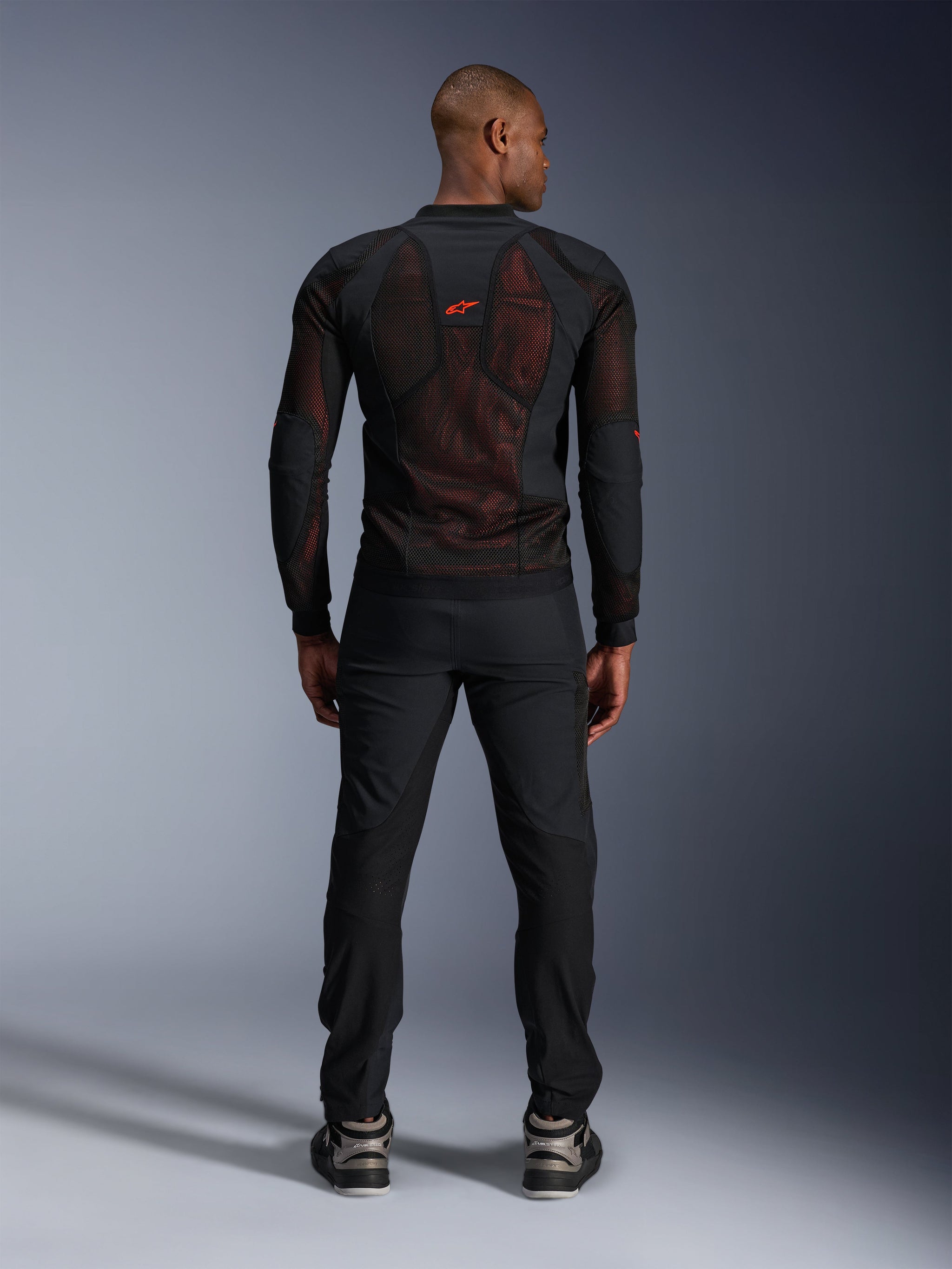 Alpinestars Troop-Air Pro Jacket in Black Red Fluo, rear view on model, technical armored mesh jacket with breathable panels, red logo on upper back, worn with black pants and sneakers, urban motorcycle apparel