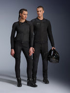 Veste Alpinestars Stella Troop-Air, homme et femme portant un équipement de moto technique assorti tout en noir, doté d'une construction en maille pour la circulation de l'air, pantalons et bottes noirs, homme tenant un casque noir, tenue de moto urbaine