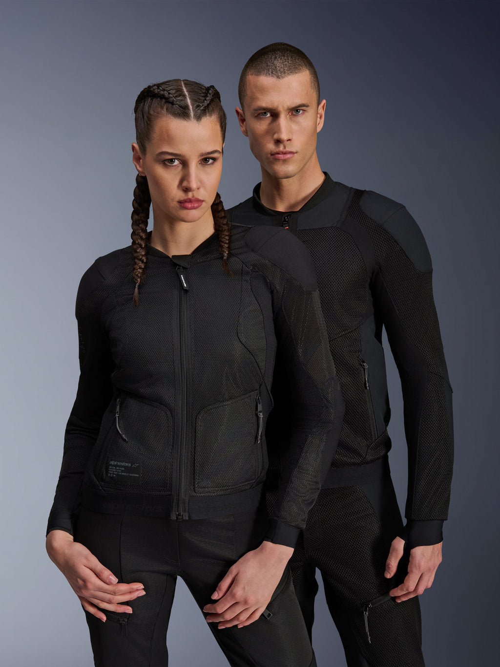 Veste Alpinestars Troop-Air Pro, vestes techniques blindées noires portées par des modèles homme et femme, dotées de panneaux en mesh respirant et d'une protection intégrée, équipement de moto urbain conçu pour la conduite par temps chaud.