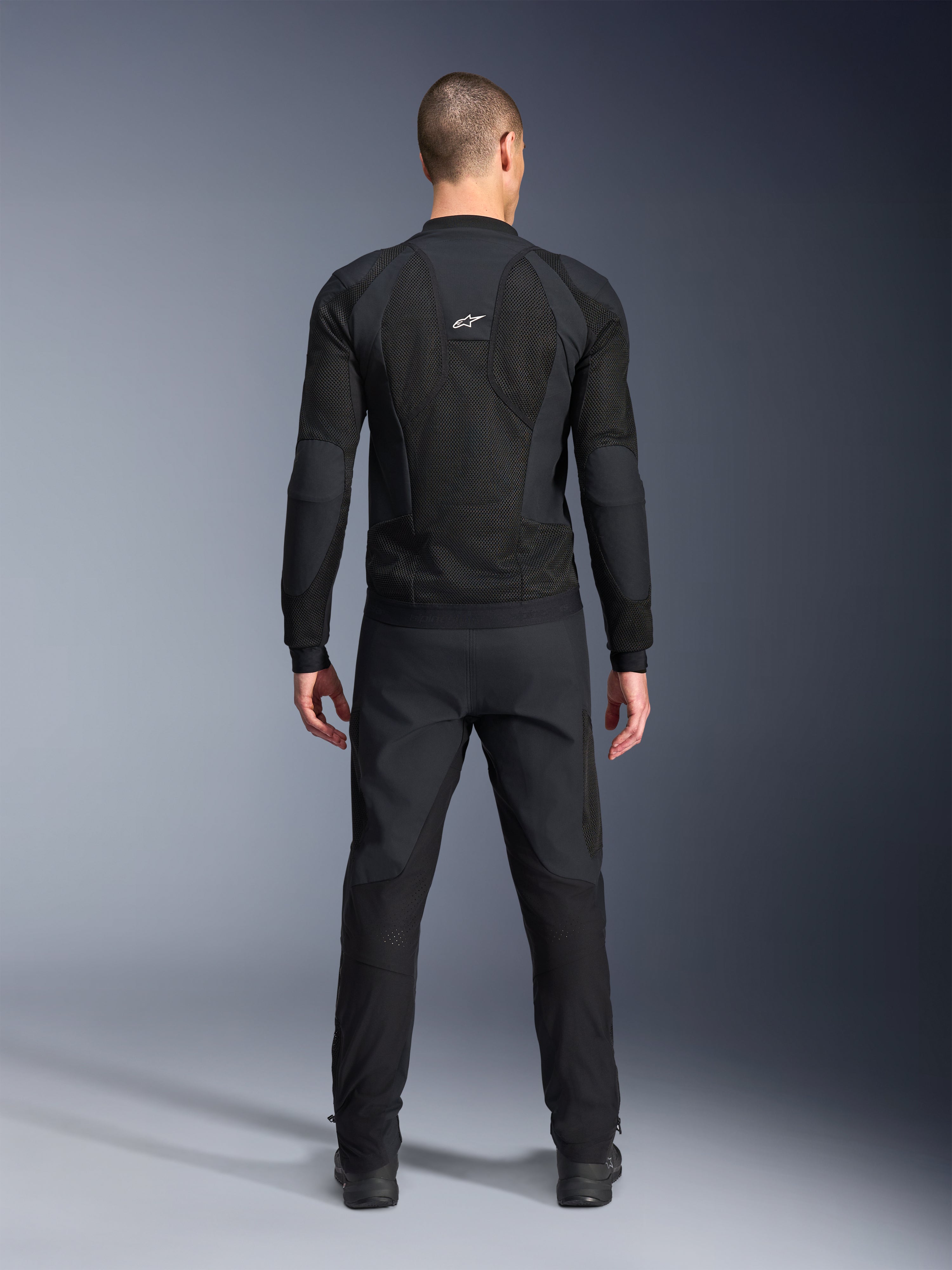Veste Alpinestars Troop-Air Pro, vue arrière, noir, veste de moto technique aérée dotée de larges panneaux de ventilation en maille et d'un logo Alpinestars blanc, associée à un pantalon noir, équipement de moto urbain contemporain