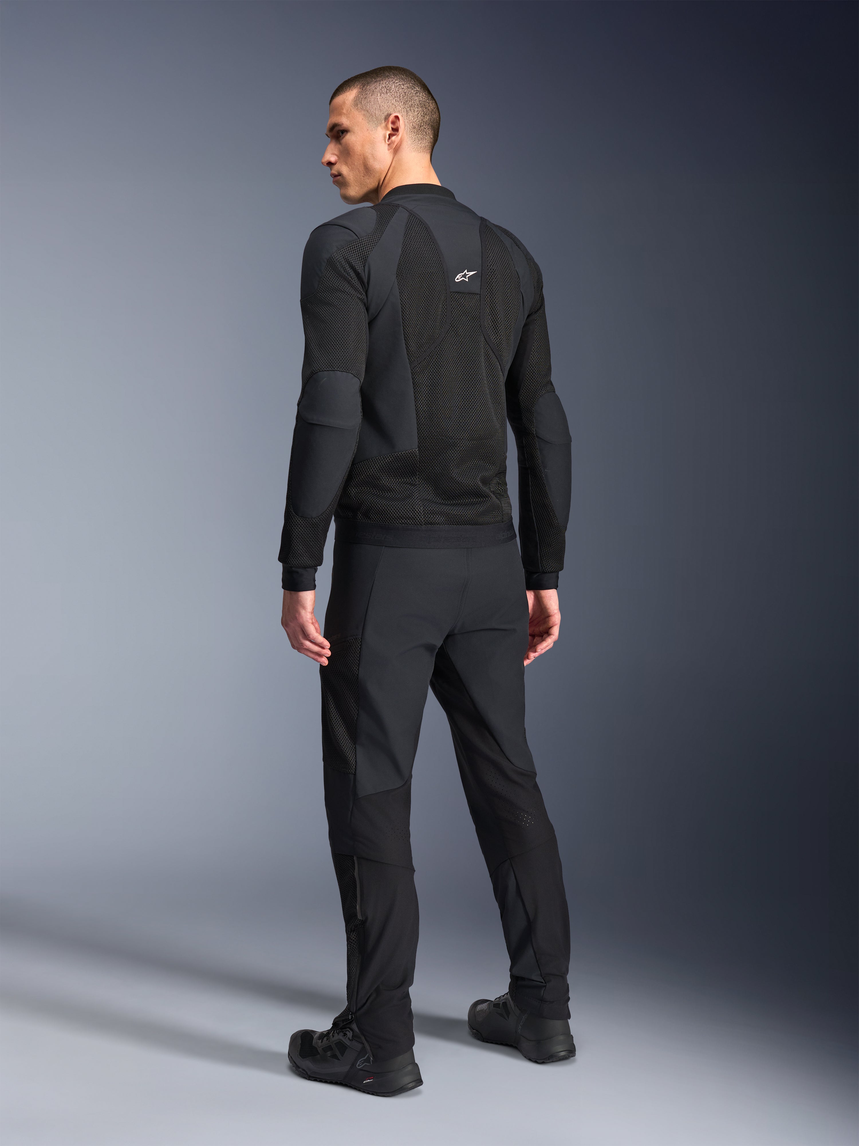 Veste Alpinestars Troop-Air Pro, noire, veste technique blindée et ventilée vue de dos, avec de larges panneaux en mesh pour la circulation de l'air, accompagnée d'un pantalon technique et de chaussures noirs assortis.