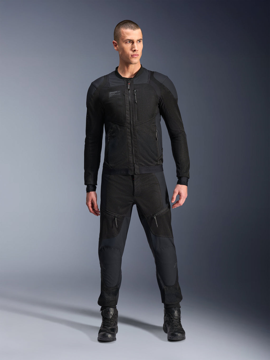 Veste Alpinestars Troop-Air Pro, veste de moto technique blindée noire, dotée de panneaux en mesh et de fermetures éclair à l'avant, portée avec un pantalon noir assorti et des bottes de moto, équipement de route urbain haut de gamme