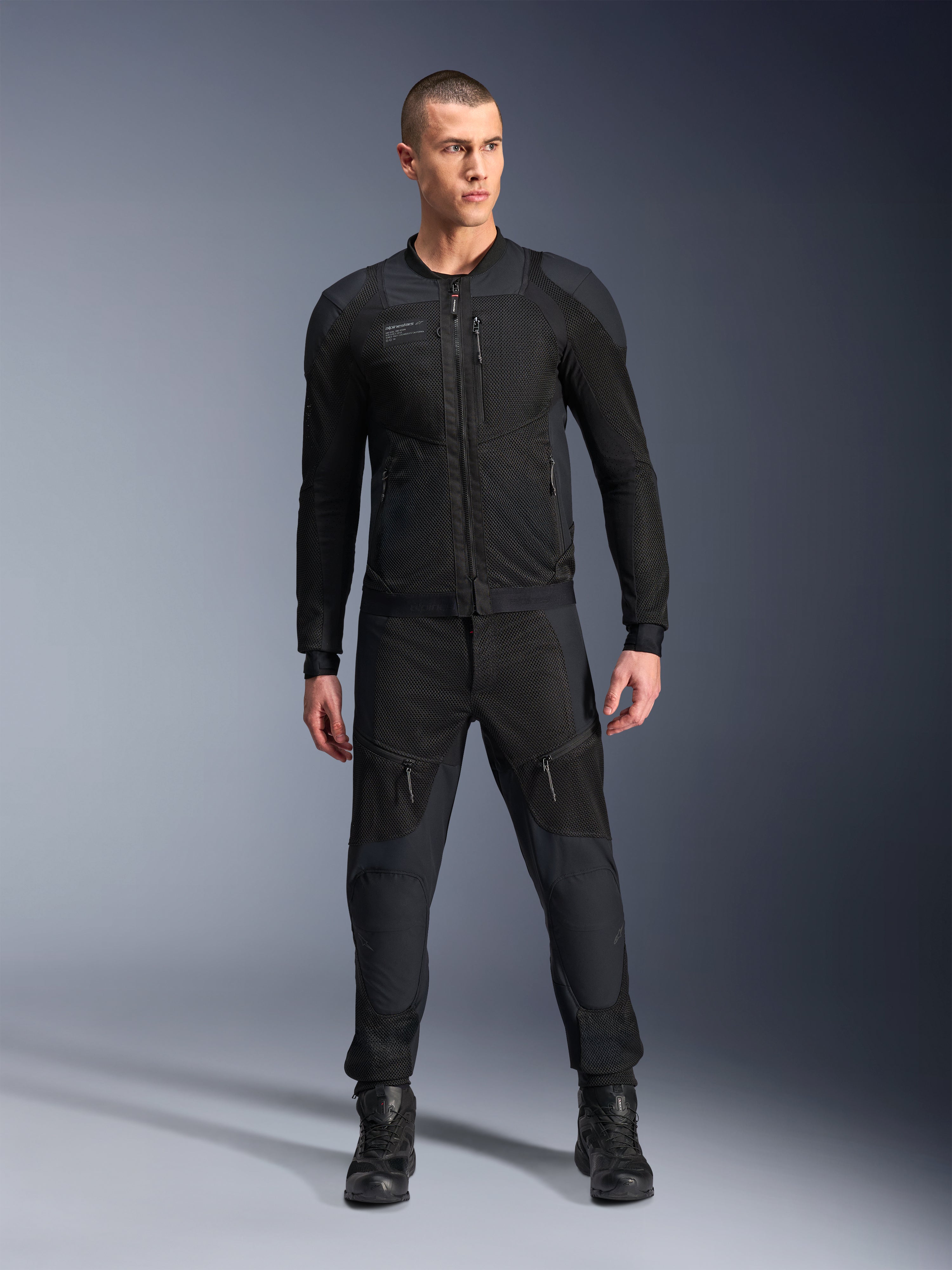 Veste Alpinestars Troop-Air Pro, veste de moto technique blindée noire, dotée de panneaux en mesh et de fermetures éclair à l'avant, portée avec un pantalon noir assorti et des bottes de moto, équipement de route urbain haut de gamme