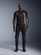 Mannequin homme portant la veste Alpinestars Troop-Air en Noir Gris Cendré et Rouge Vif, veste de moto technique en maille présentant un logo rouge proéminent sur la poitrine, assortie d'un pantalon et de bottes de moto noirs, tenue de route urbaine