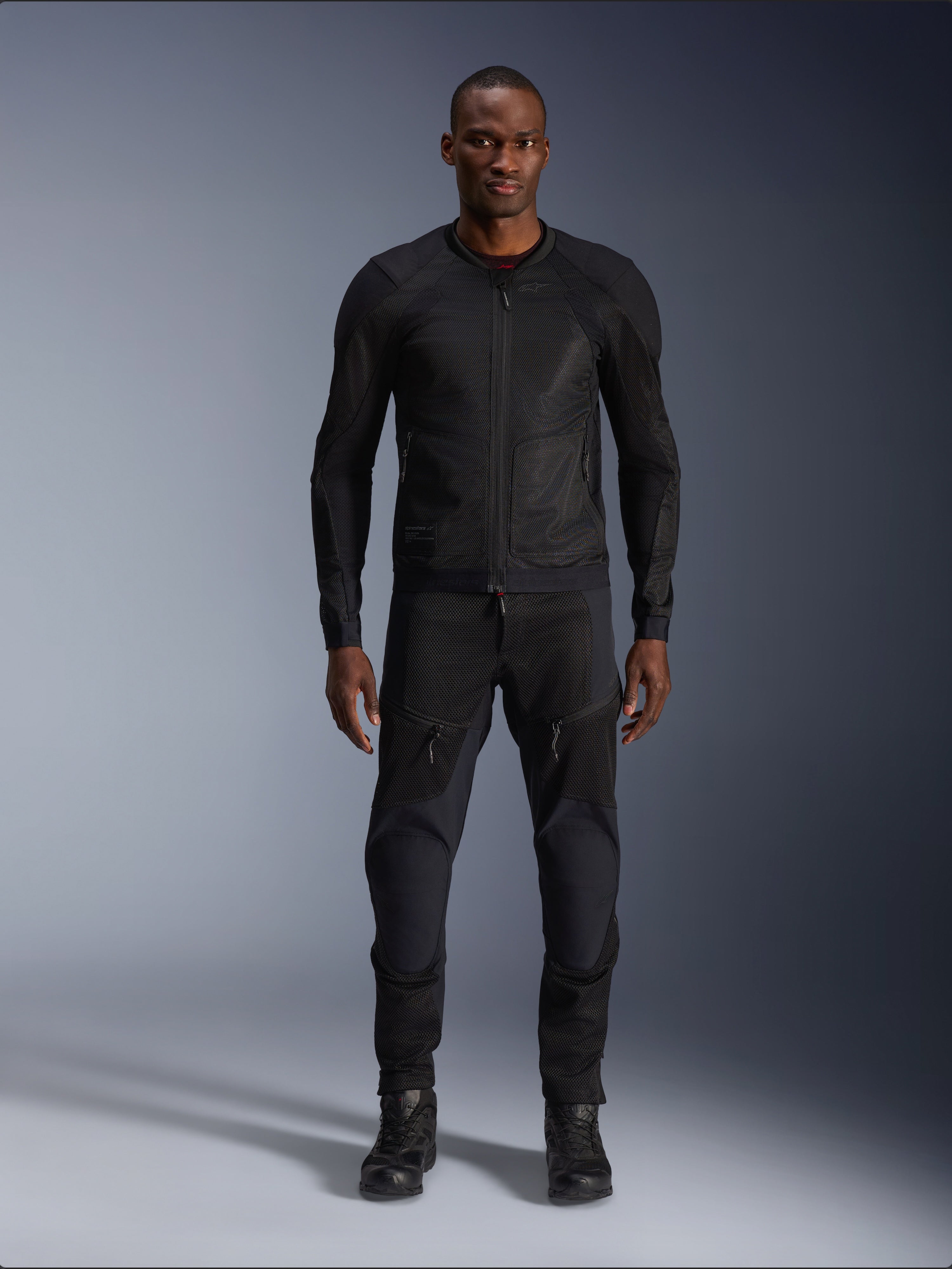 Modèle masculin portant la veste Alpinestars Troop-Air en coloris Black Black, veste de moto légère en mesh, associée à un pantalon et des bottes de moto noirs assortis, dotée d'une construction technique en maille 2D pour un flux d'air supérieur.