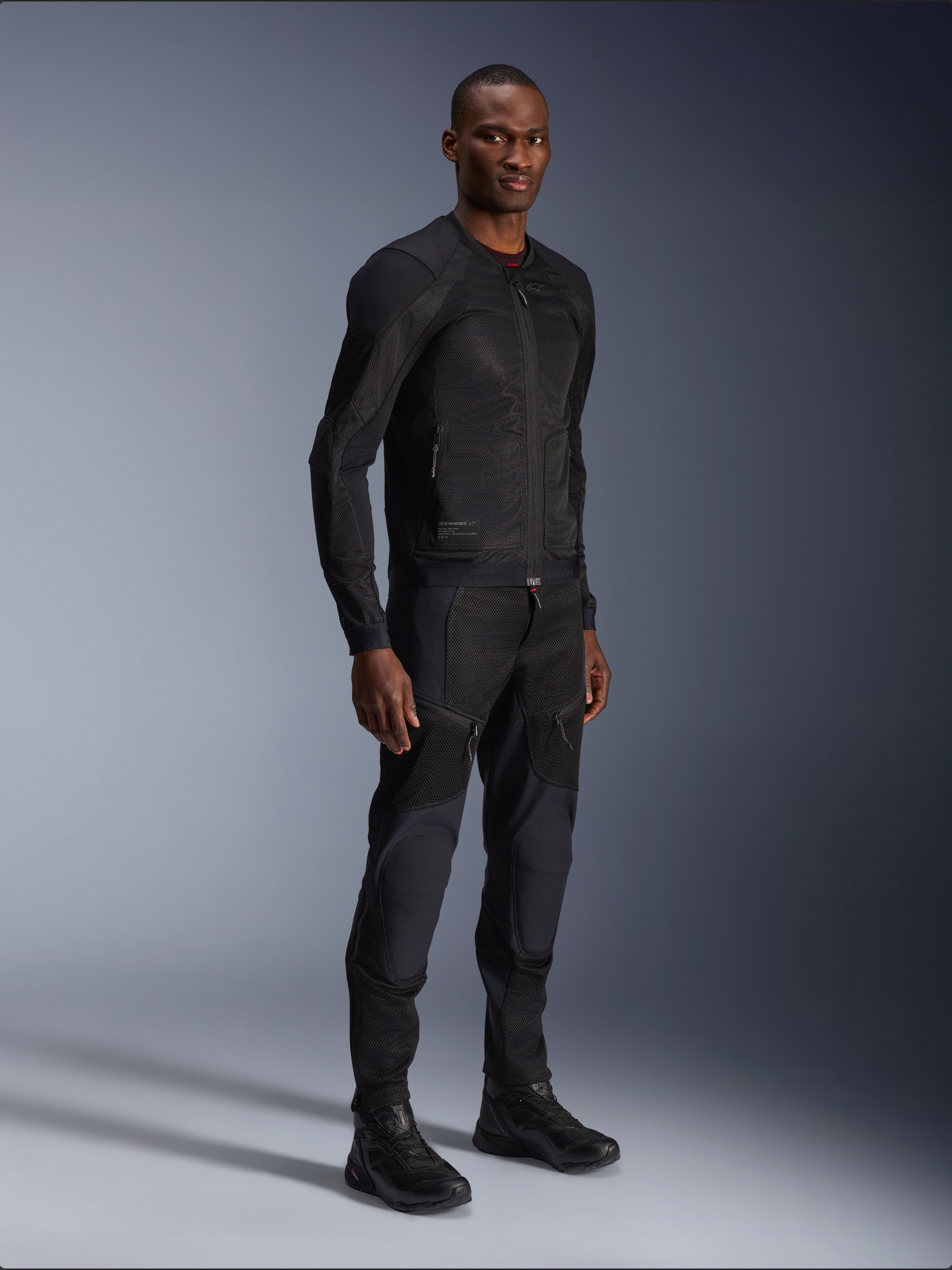 Veste Alpinestars Troop-Air, noire, veste de moto technique en maille portée par un mannequin avec un pantalon et des bottes noirs assortis, dotée d'une construction en maille légère et d'un design urbain minimaliste