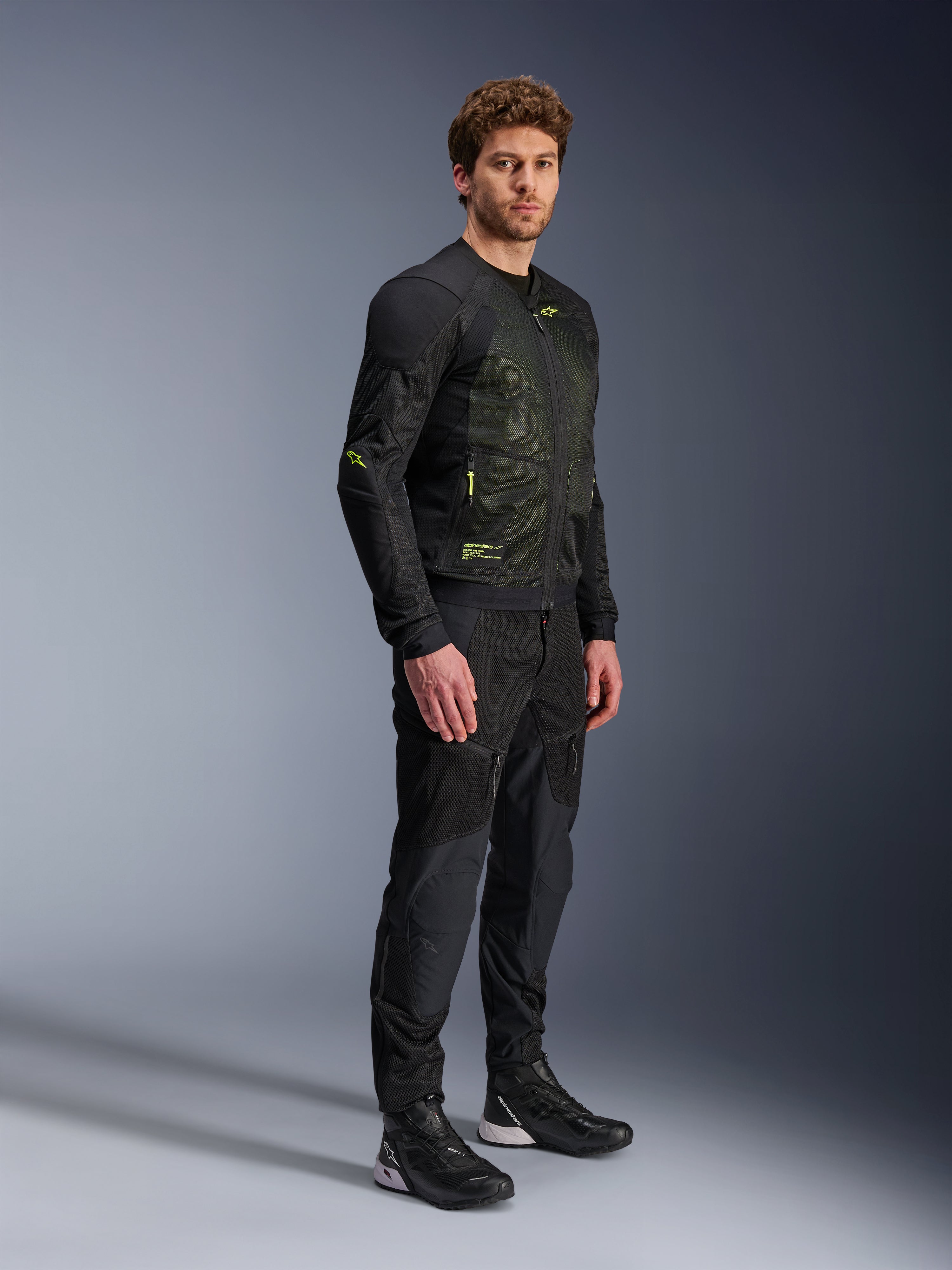 Alpinestars Troop-Air Jacket, Motorcycle Mesh Jacket, Black and Yellow Fluo, worn by a model with matching black pants and riding shoes, features high-airflow mesh construction with yellow fluorescent accents on the chest and sleeves, lightweight technical design for road riding