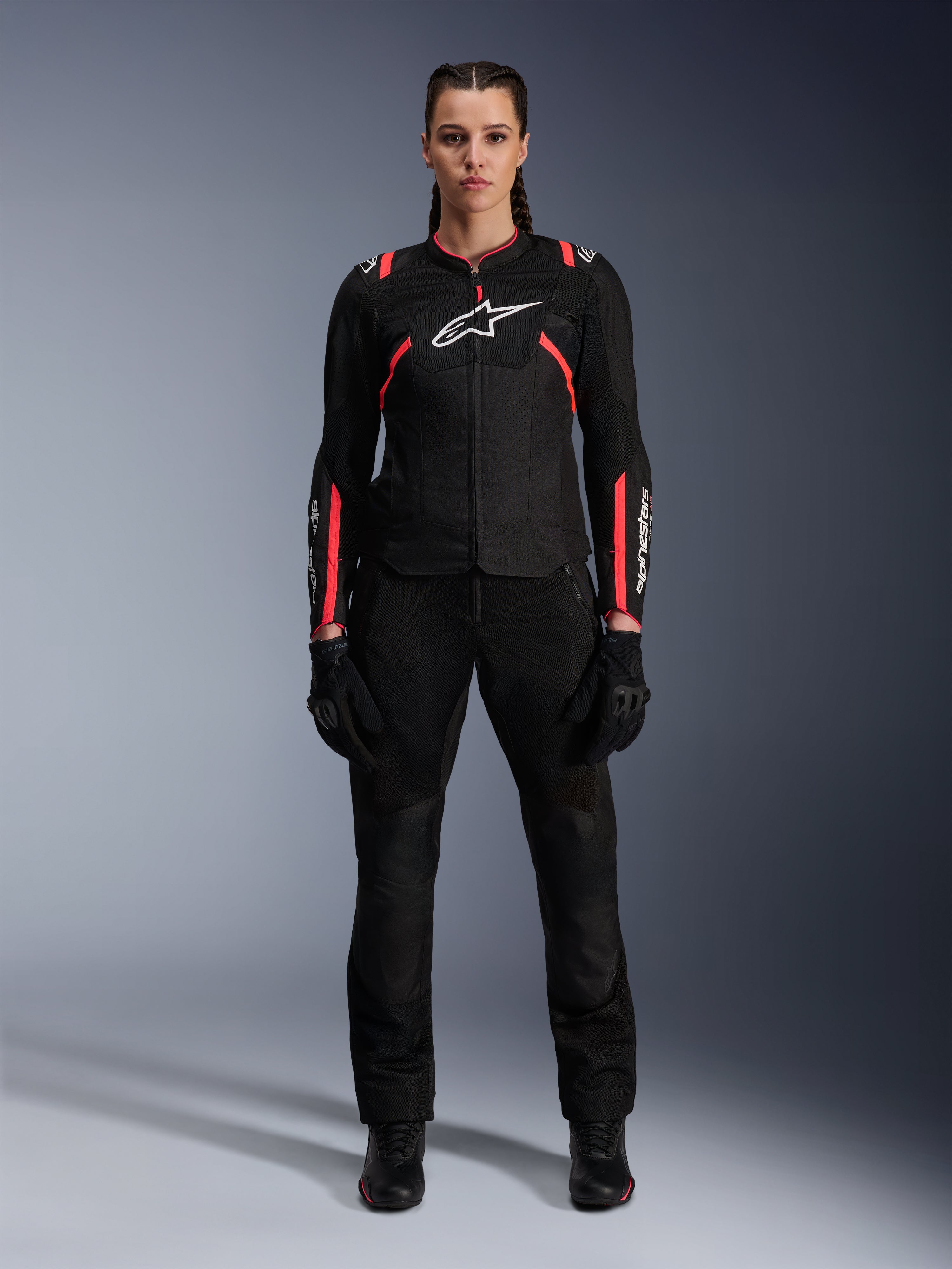 Veste Alpinestars Stella T-SPS Air v2, veste de moto pour femme, noir et rose Diva, vue de face, logo blanc sur la poitrine, panneaux de ventilation en mesh, portée avec un pantalon et des gants noirs, équipement de conduite urbain élégant
