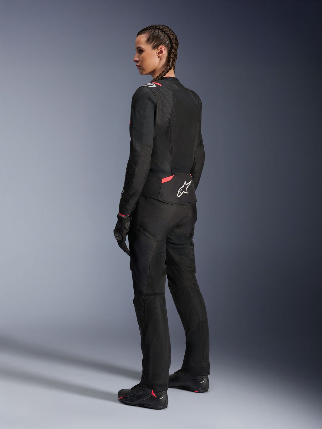 Veste Alpinestars Stella T-SPS Air v2 pour femme, noir et rose diva, veste de moto en textile vue de trois-quarts arrière, dotée de grands panneaux en mesh pour la ventilation et d'un logo étoile blanc au dos, portée avec un pantalon, des gants et des bottes de moto noirs assortis.