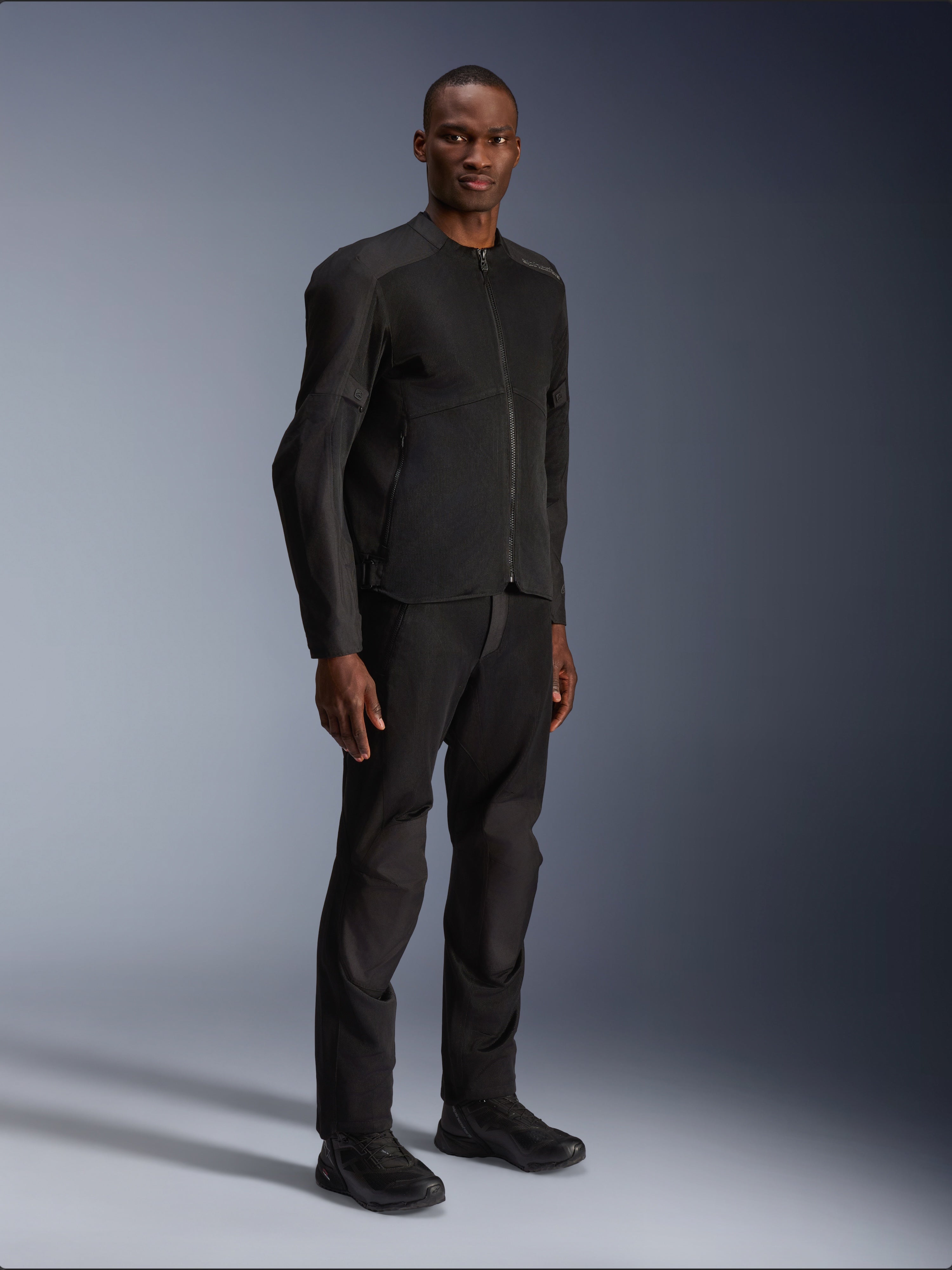 Veste Alpinestars C-1 Air, noir, portée par un mannequin avec pantalon et chaussures de moto noirs assortis, dotée de larges panneaux en maille technique pour la circulation de l'air, esthétique urbaine épurée avec une coupe profilée