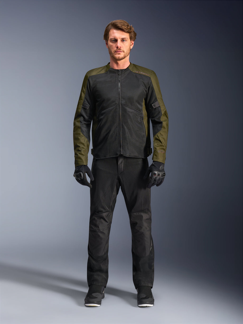 Veste Alpinestars C-1 Air, kaki et noir, portée par un mannequin homme avec un pantalon de moto et des gants noirs, conception textile légère avec panneaux en maille technique, équipement de conduite urbain contemporain