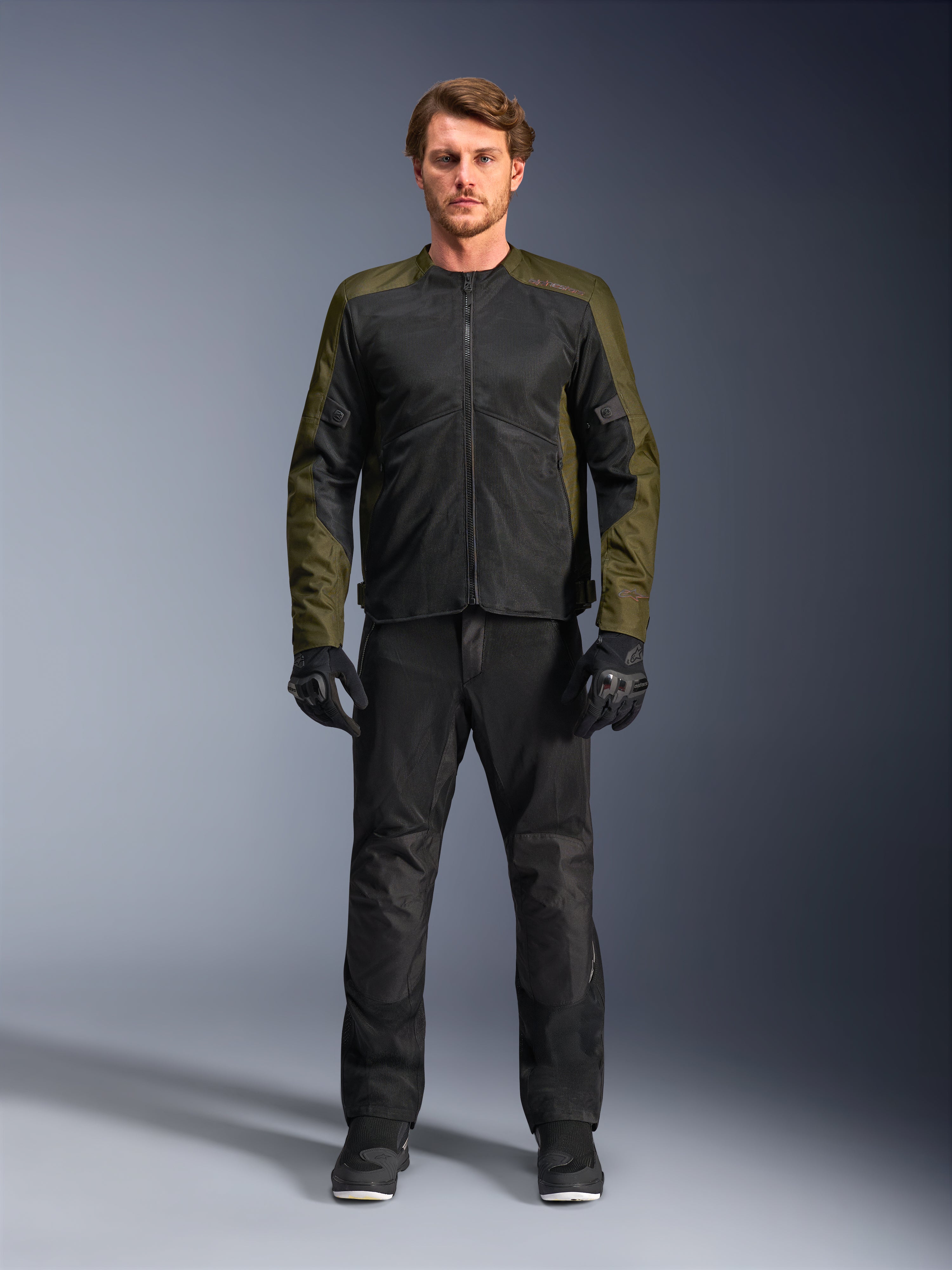 Veste Alpinestars C-1 Air, kaki et noir, portée par un mannequin homme avec un pantalon de moto et des gants noirs, conception textile légère avec panneaux en maille technique, équipement de conduite urbain contemporain
