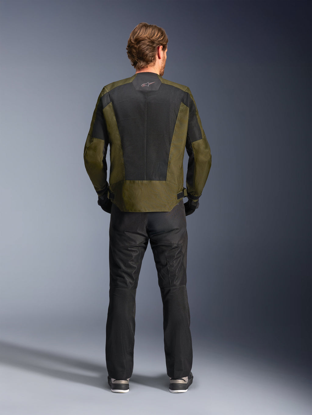 Vue arrière d'un motard portant la veste Alpinestars C-1 Air en kaki et noir, dotée d'un grand panneau arrière en maille technique pour la ventilation, associée à un pantalon de moto noir, équipement de route urbain contemporain