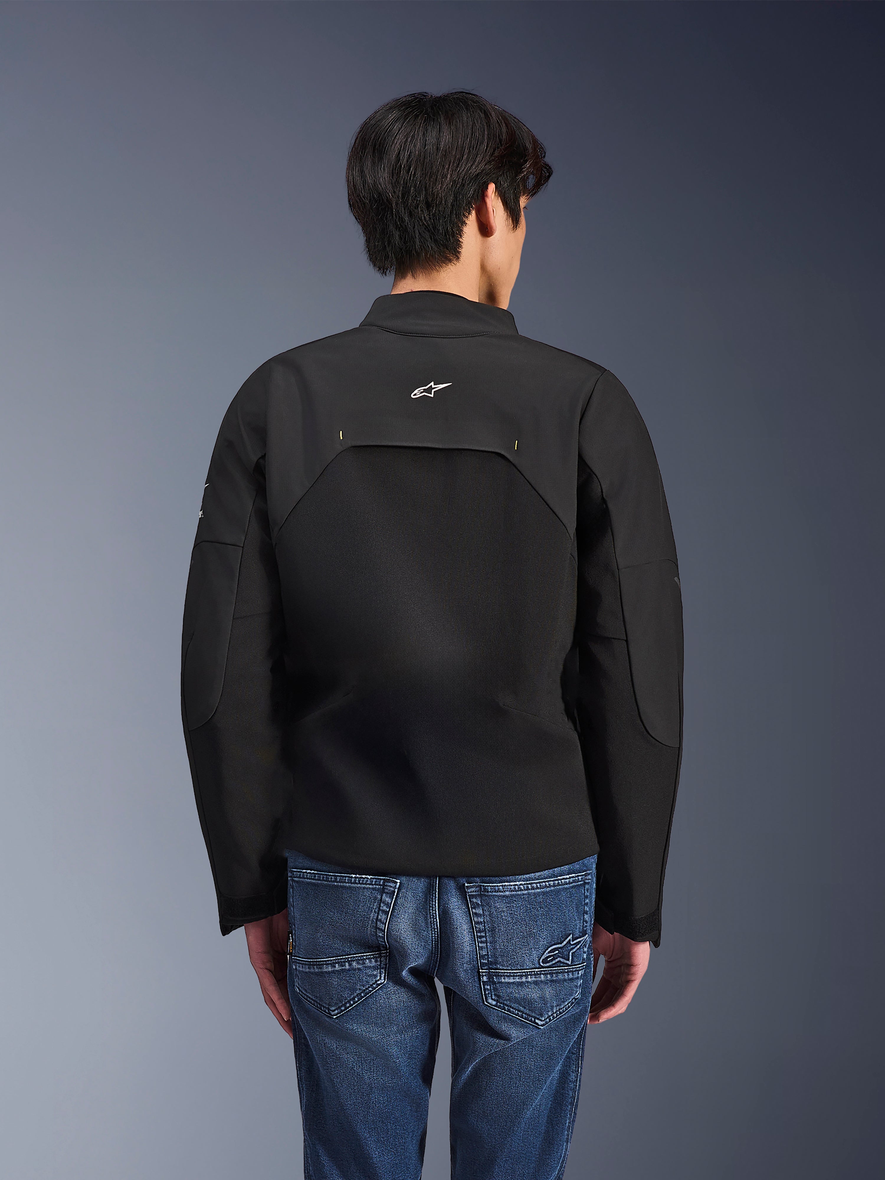 Veste Alpinestars Provoke, veste de moto urbaine, noire, vue arrière montrant le logo Astars blanc et des panneaux techniques en ripstop, portée avec un jean bleu, design contemporain pour les trajets urbains