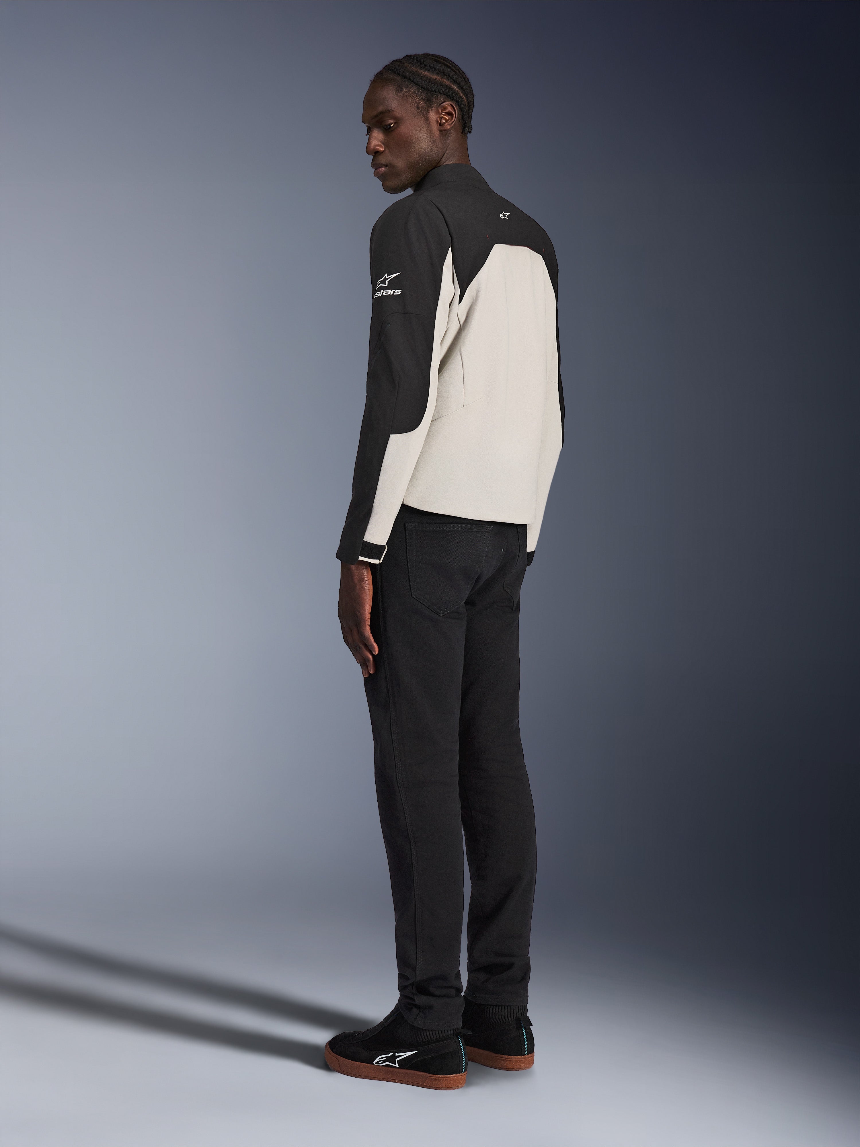 Veste Alpinestars Provoke, veste de moto urbaine, noir et gris métal, vue de trois-quarts arrière sur un mannequin, construction textile bicolore avec logo Alpinestars sur l'épaule, portée avec un pantalon noir et des baskets noires, protection contemporaine pour la conduite urbaine
