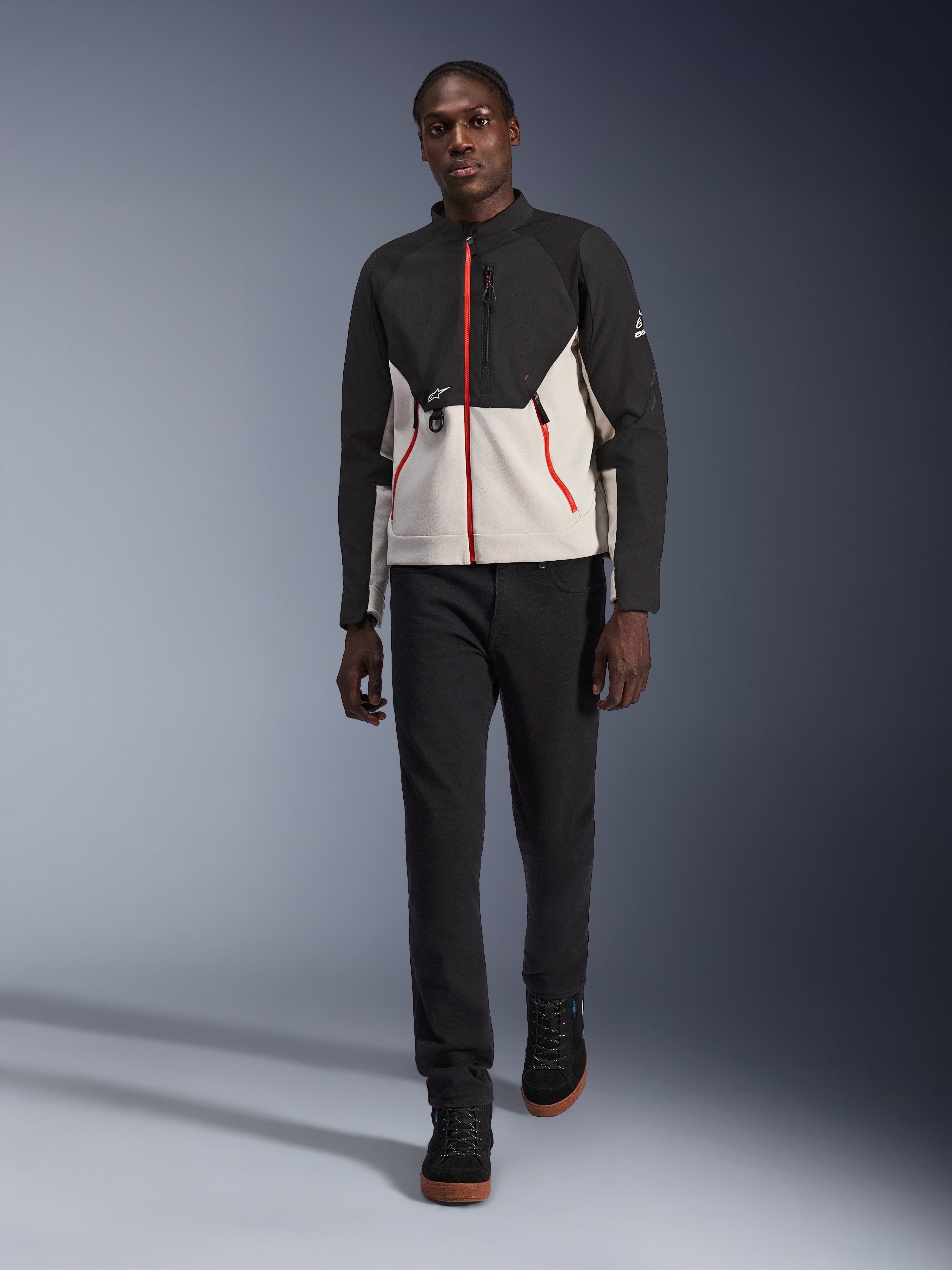 Mannequin portant la veste Alpinestars Provoke, veste de moto urbaine noir et gris métal avec des accents de zips rouges, accompagnée d'un pantalon noir et de chaussures montantes noires, équipement de protection moderne pour la conduite urbaine