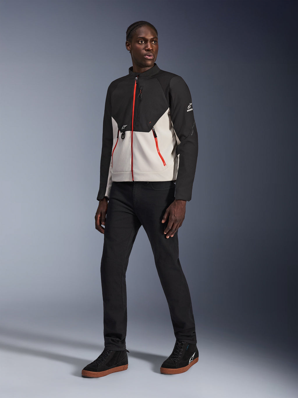 Mannequin portant la veste Alpinestars Provoke en Black Metal Gray, avec des fermetures éclair rouges distinctives sur le devant et les poches, associée à un pantalon noir et des baskets montantes noires avec des semelles en gomme, équipement de moto urbain contemporain pour un look prêt pour la rue.