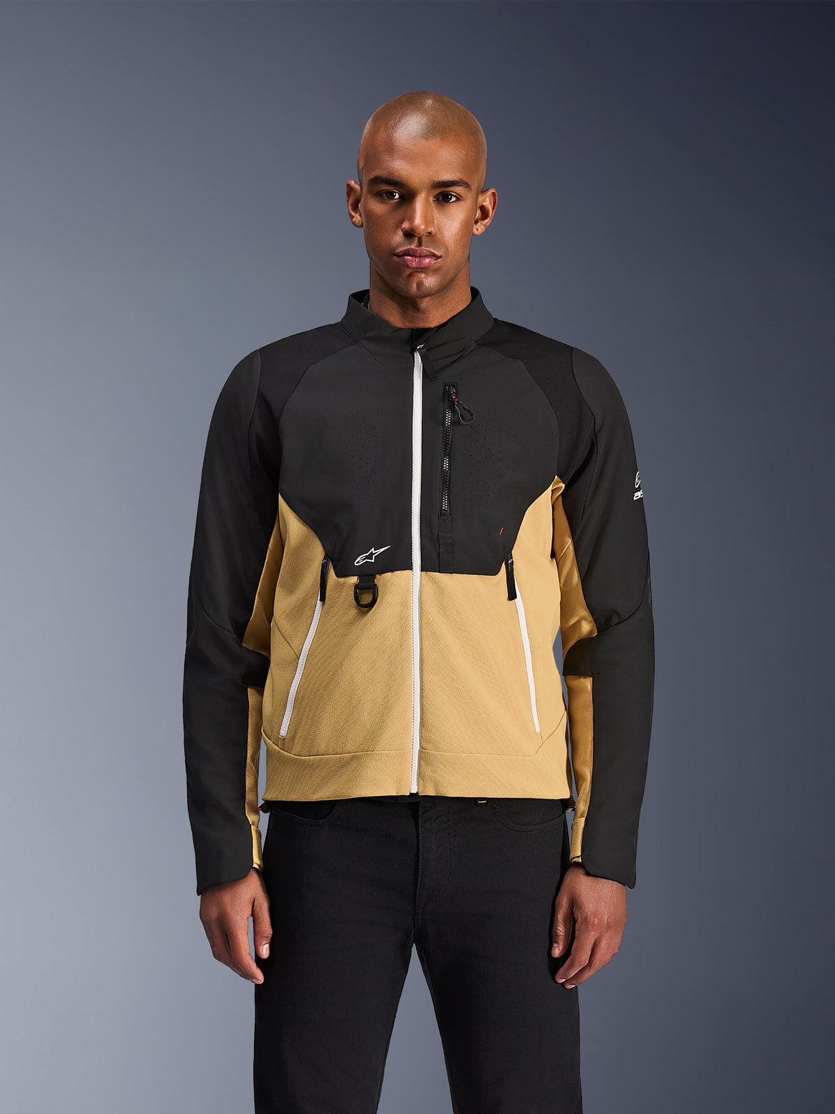 Veste Alpinestars Provoke, veste de moto urbaine, noir et camel, vue de face sur un mannequin homme, design bicolore avec fermetures éclair blanches, poche poitrine zippée avec anneau en D et petit logo Alpinestars blanc, tenue de motard urbaine contemporaine