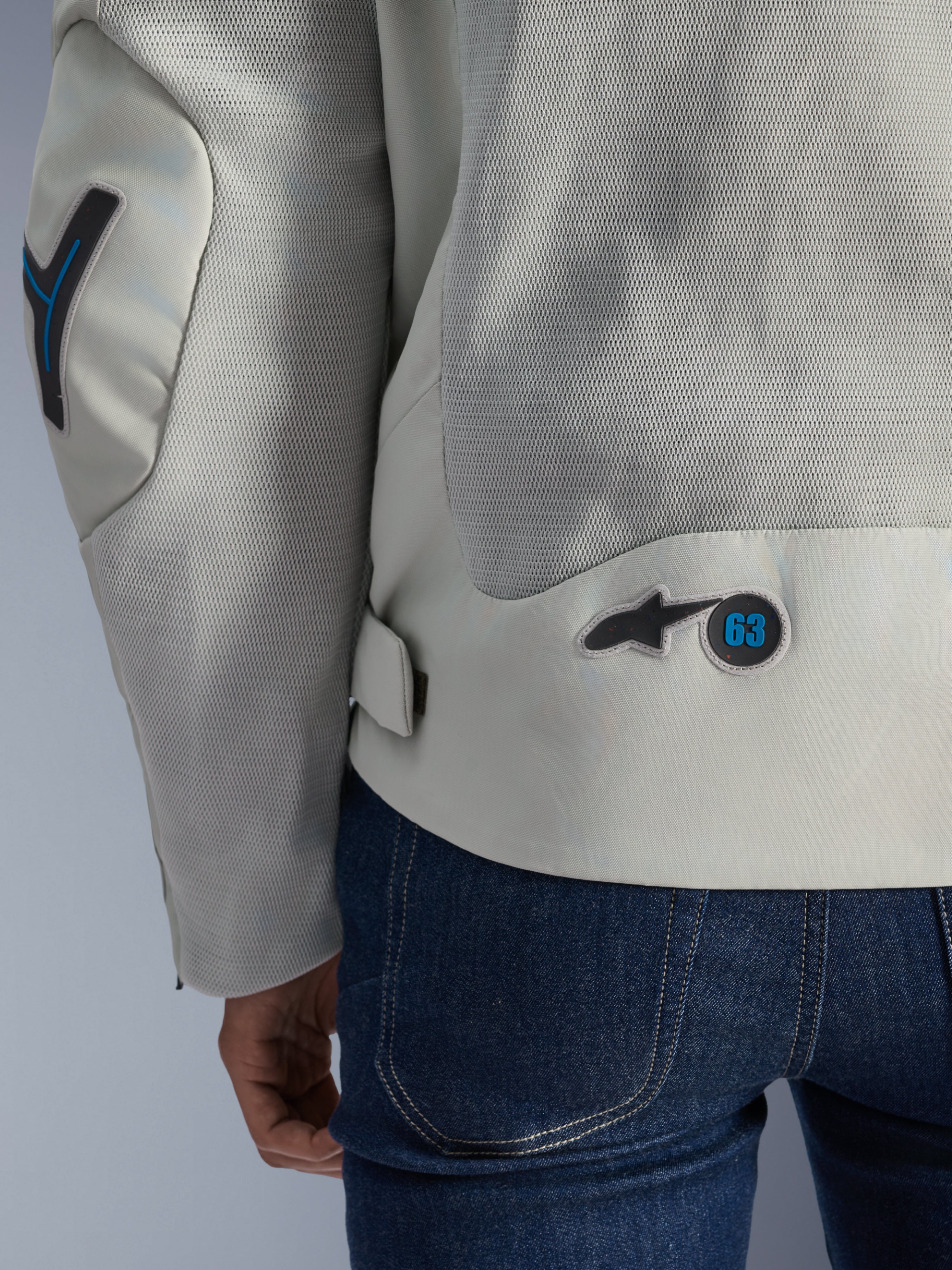 Veste Alpinestars Circal-1 Air en gris métal avec accents bleu méthyle, vue arrière détaillée mettant en avant les panneaux de flux d'air en maille recyclée et le badge logo circulaire « 63 », portée avec un jean bleu
