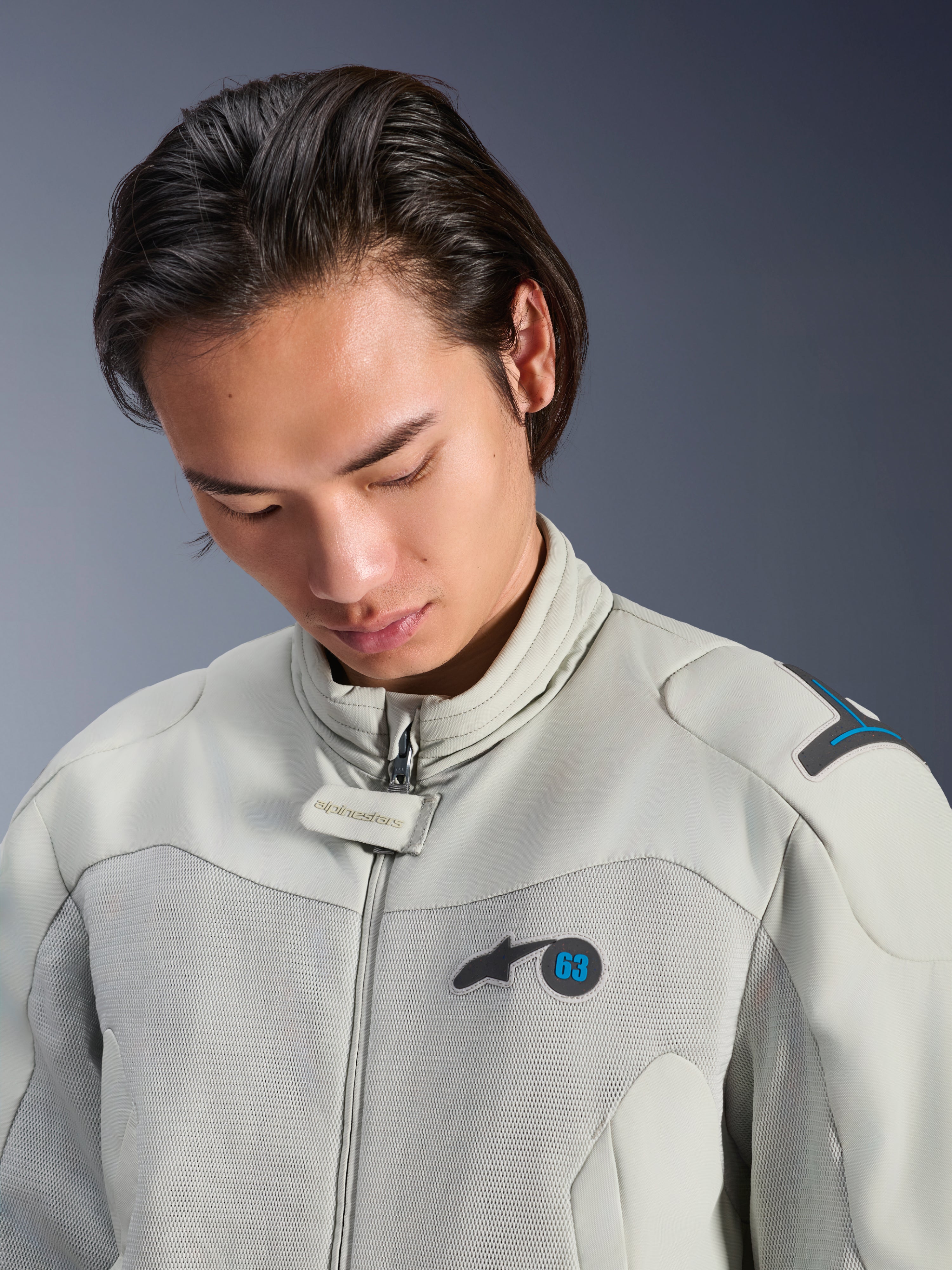 Modèle masculin portant la veste Alpinestars Circal-1 Air en gris métal avec des accents bleu méthyle, vue rapprochée mettant en avant le col, les panneaux de poitrine en maille et le logo minimaliste, équipement de moto urbain durable.