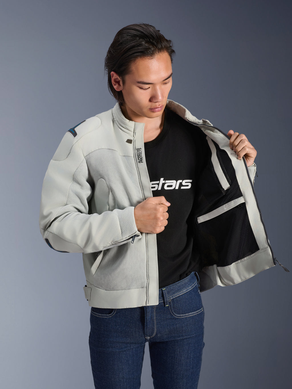 Veste Alpinestars Circal-1 Air, Gris Métal, maintenue ouverte pour montrer la doublure intérieure en maille et les détails des poches, portée par un mannequin avec un t-shirt noir à logo et un jean bleu, style moto urbain