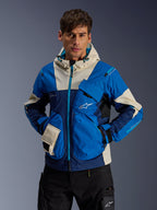 Modèle masculin portant la veste Alpinestars Mogress Air en Blue Almond, veste de moto urbaine avec blocs de couleurs bleu vif et bleu marine, accents crème sur la capuche et les poches, tissu technique ripstop avec poches utilitaires, streetwear moderne inspiré du sport automobile
