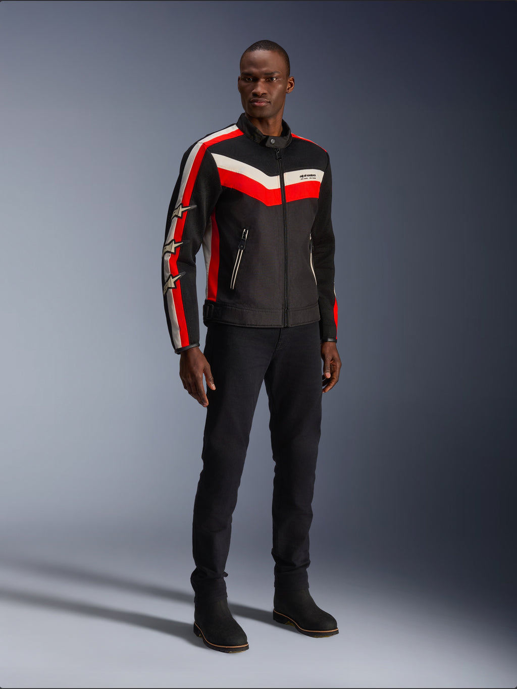 Alpinestars T-Dyno Air Jacket, Noir Rouge Éclatant Écru, veste de moto textile pour homme avec panneaux en maille 3D, présentant des bandes en chevron rouges et blanches sur la poitrine et des logos étoilés sur les manches, portée par un mannequin avec un pantalon et des bottes noirs.
