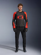 Veste Alpinestars T-Stunt Air, noir, rouge fluo et rouge foncé, portée par un mannequin avec un jean de moto noir et des gants, dotée d'une conception modulaire 2-en-1 avec des panneaux en mesh pour la circulation de l'air, équipement de moto à coupe sportive pour la route
