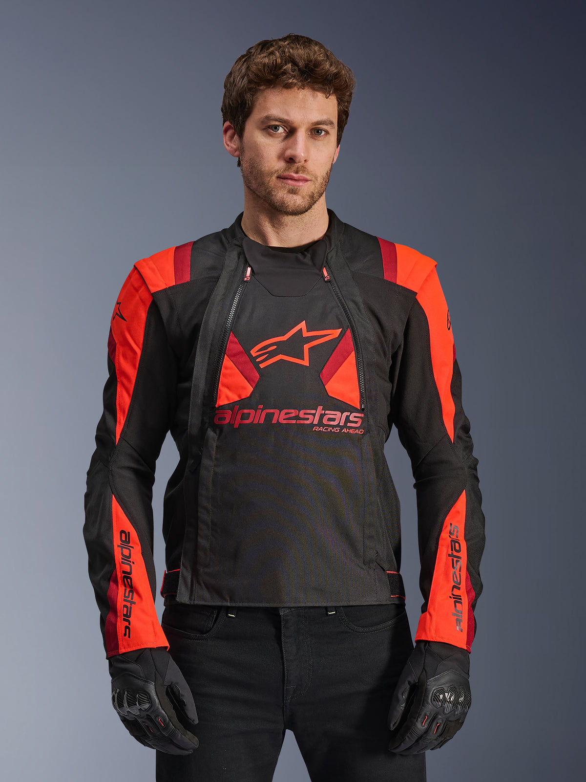 Alpinestars T-Stunt Air Jacket, veste de moto en textile, noir, rouge fluo et rouge foncé, avec un grand logo étoile et des panneaux en maille pour la circulation de l'air, portée par un mannequin avec des gants noirs