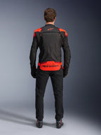 Veste Alpinestars T-Stunt Air, noire avec accents Rouge Fluo et Rouge Foncé, vue de dos sur modèle, accompagnée d'un pantalon de moto et de bottes noirs, arborant un marquage Alpinestars imposant sur le bas du dos, conception modulaire avec mesh pour la ventilation.