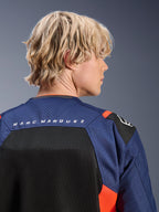 Veste Alpinestars MM93 T-SPS Air V2, bleu marine et noir avec des accents rouge fluo, gros plan sur le haut du dos arborant le logo 'MARC MARQUEZ', panneaux en mesh respirant et construction en textile perforé, portée par un mannequin blond.