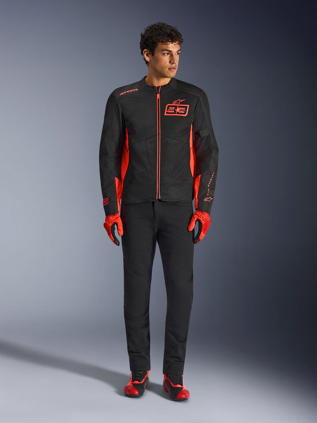 Veste de moto Alpinestars MM93 C-1 Air, noir et rouge fluo, avec marquage Marc Marquez et logo 93, portée par un mannequin avec gants rouges et pantalon noir, construction légère en textile et maille pour la conduite urbaine